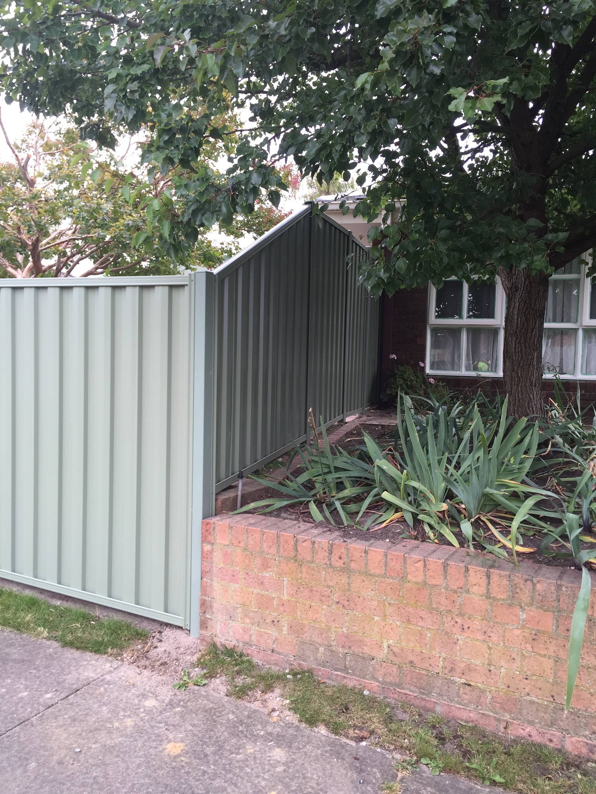 A green fence is surrounding a brick wall and a house — Aztech Fencing In Upsalls Creek, NSW