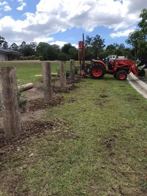 A Red Tractor is Working on Installing a Fence in a Grassy Field — Aztech Fencing In Kew, NSW