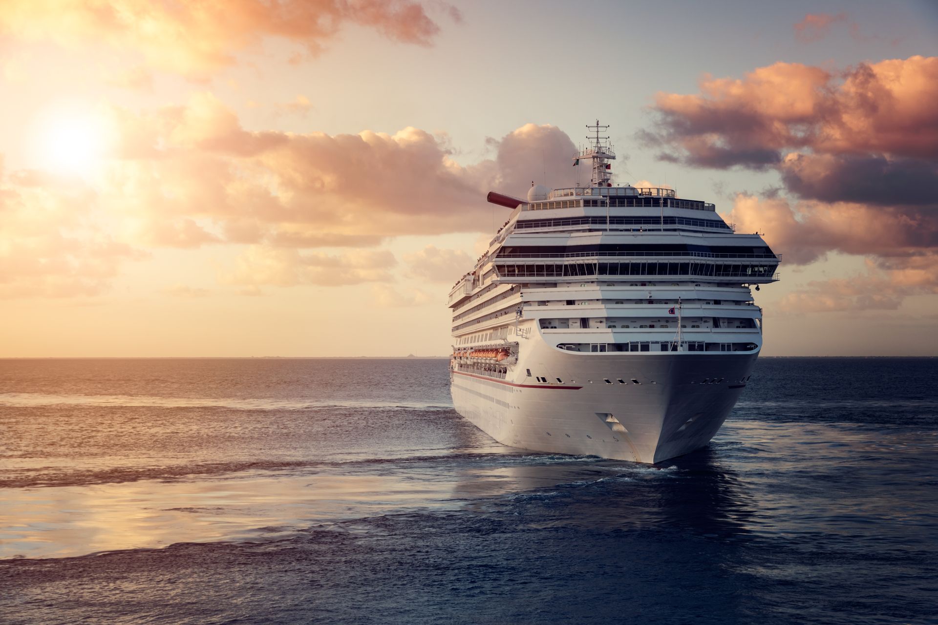 A large white cruise ship sailing on the ocean during a golden sunset with cloudy skies.