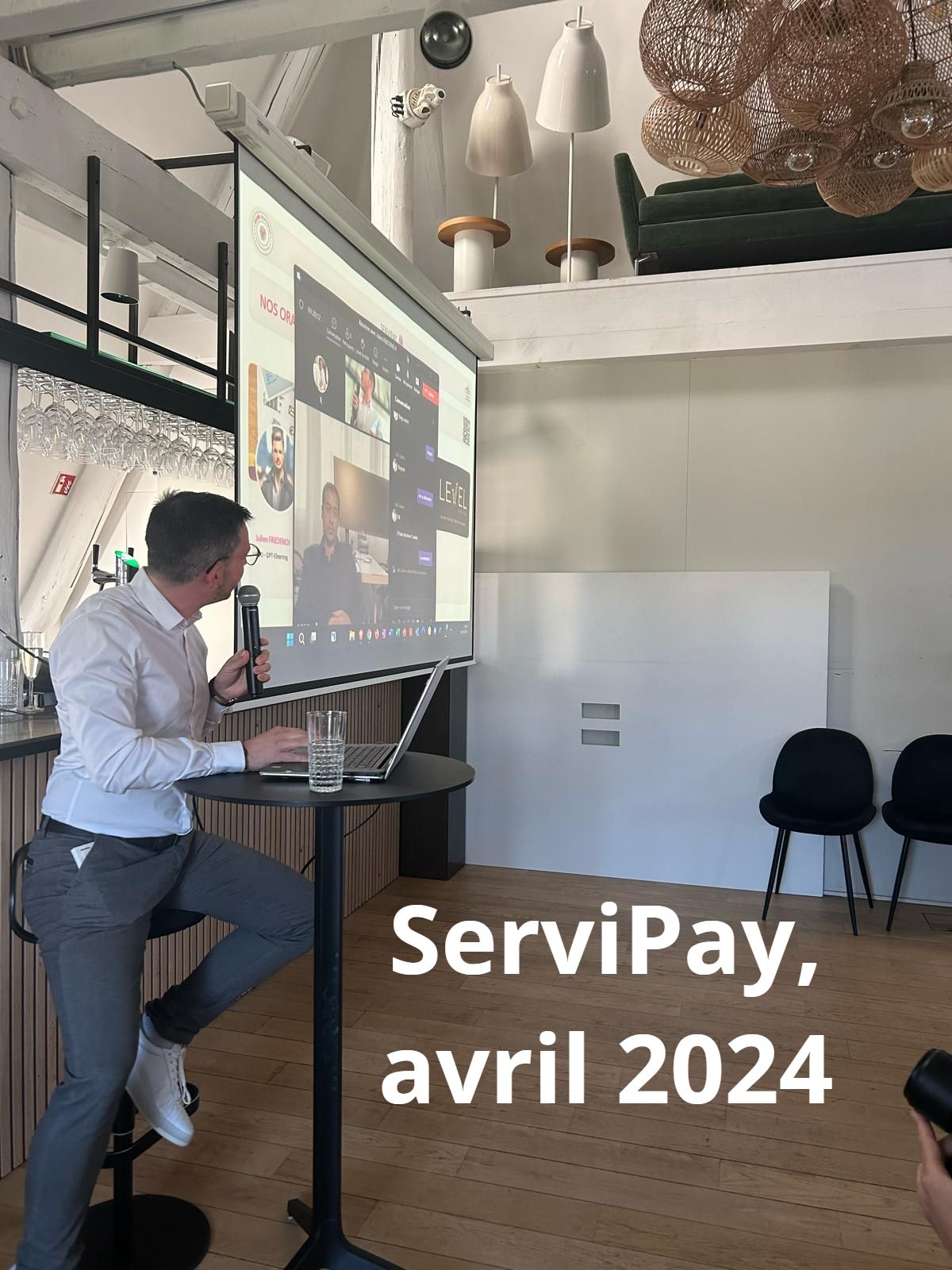 Un homme présente lors d'un événement Servipay en avril 2024. Il parle dans un microphone tout en regardant un écran affichant un appel vidéo.