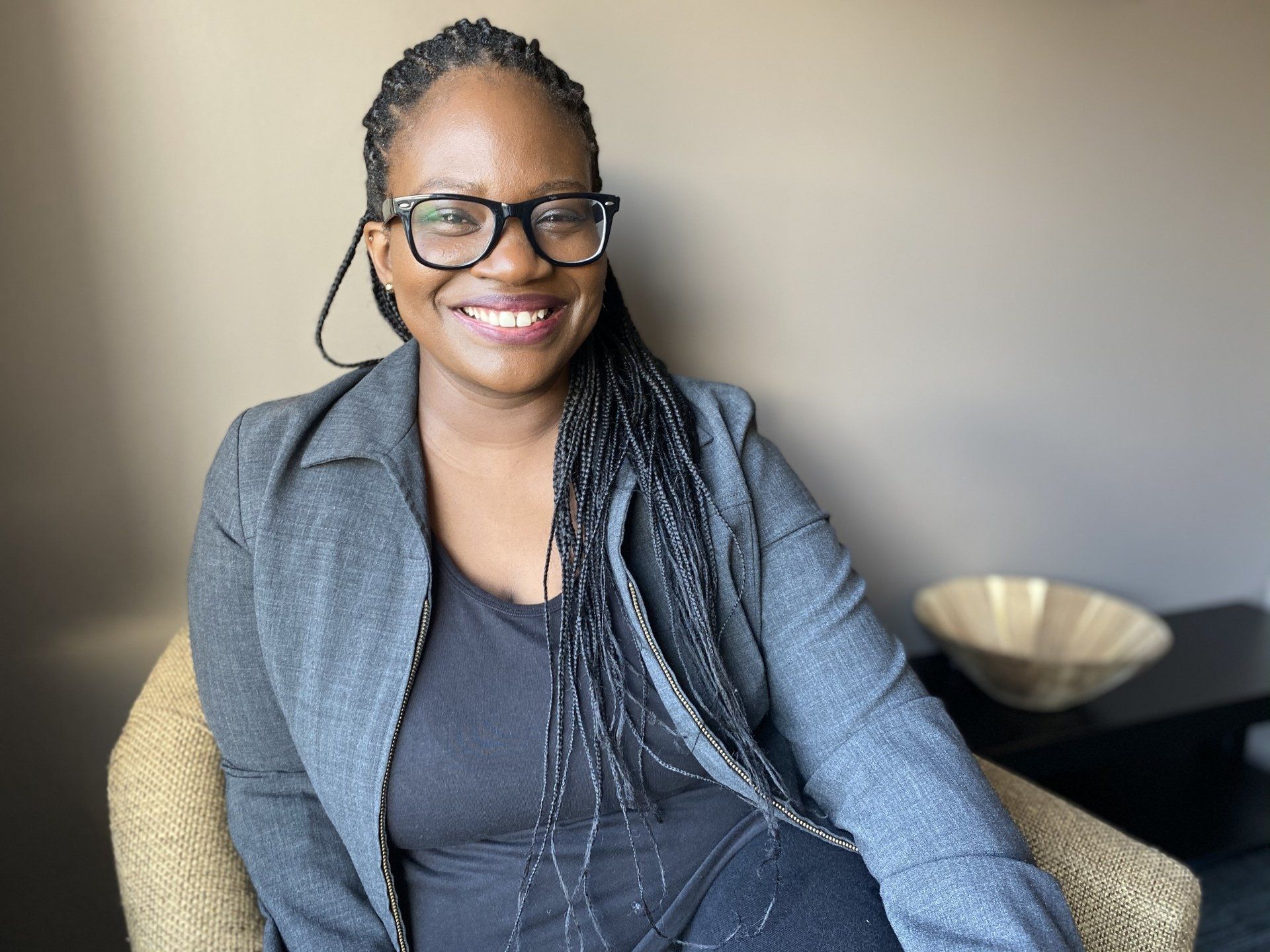 A woman wearing glasses is sitting in a chair and smiling.