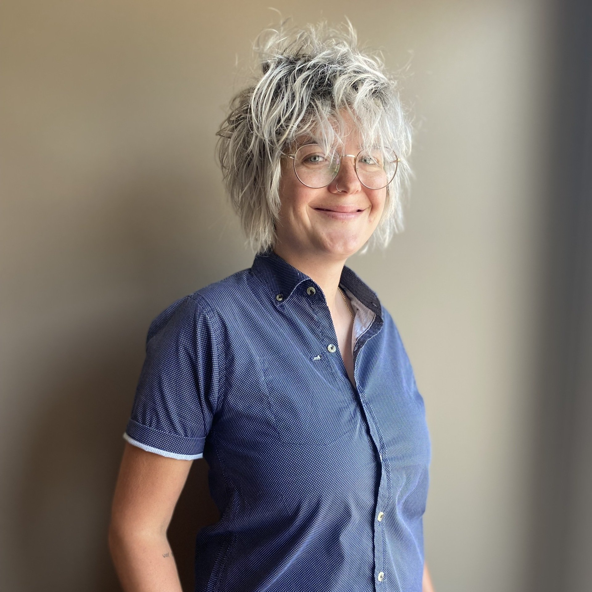 A woman wearing glasses and a blue shirt is smiling.