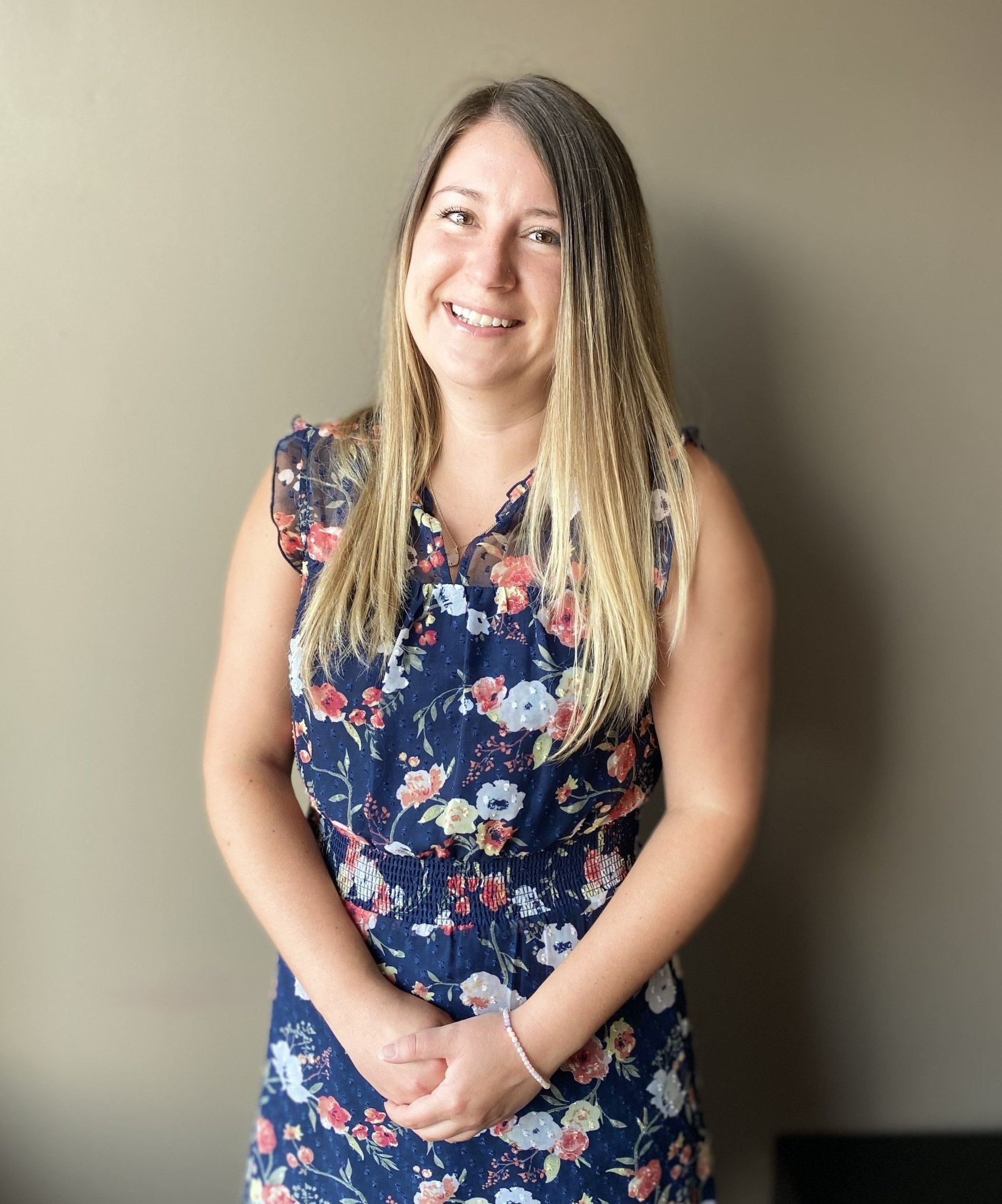 A woman in a blue floral dress is smiling for the camera.