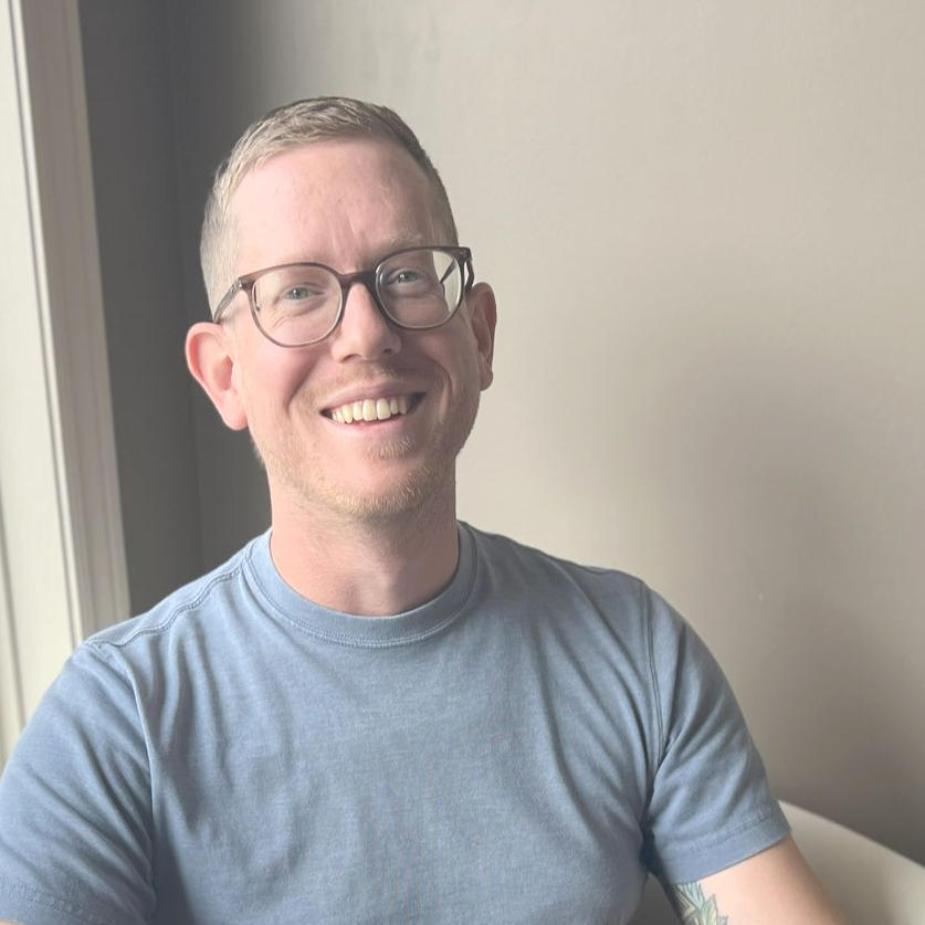A man wearing glasses and a striped shirt is smiling