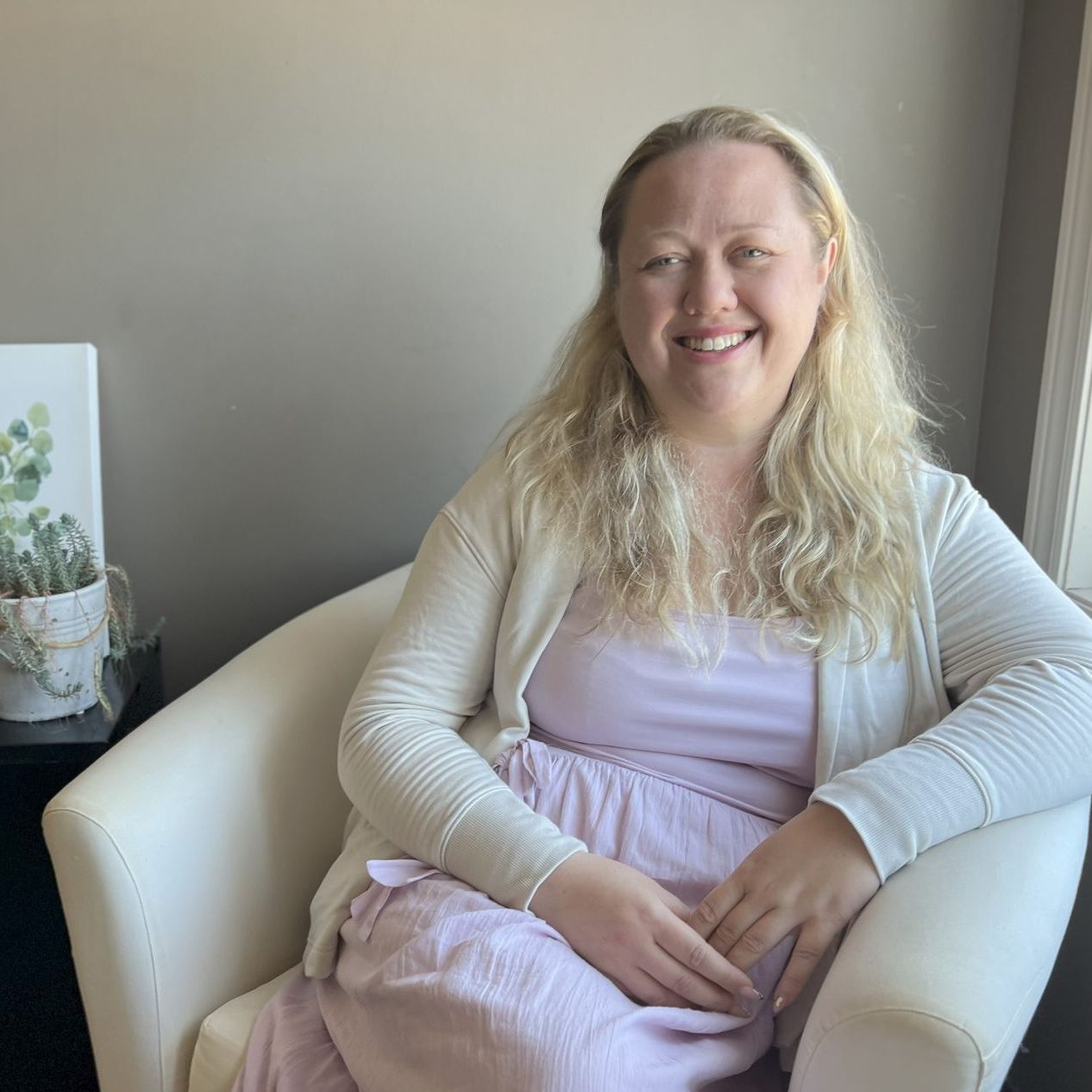 A woman in a blue shirt is smiling while sitting in a chair.