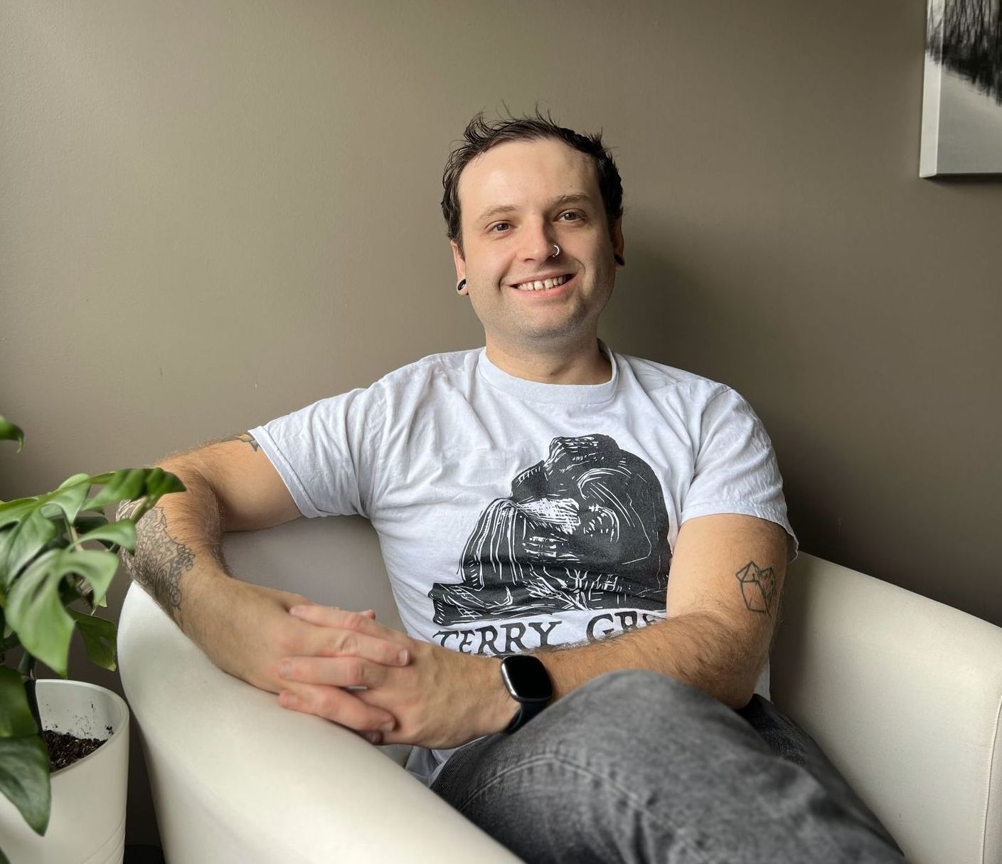 A man in a black sweater is sitting in a white chair with his hands folded