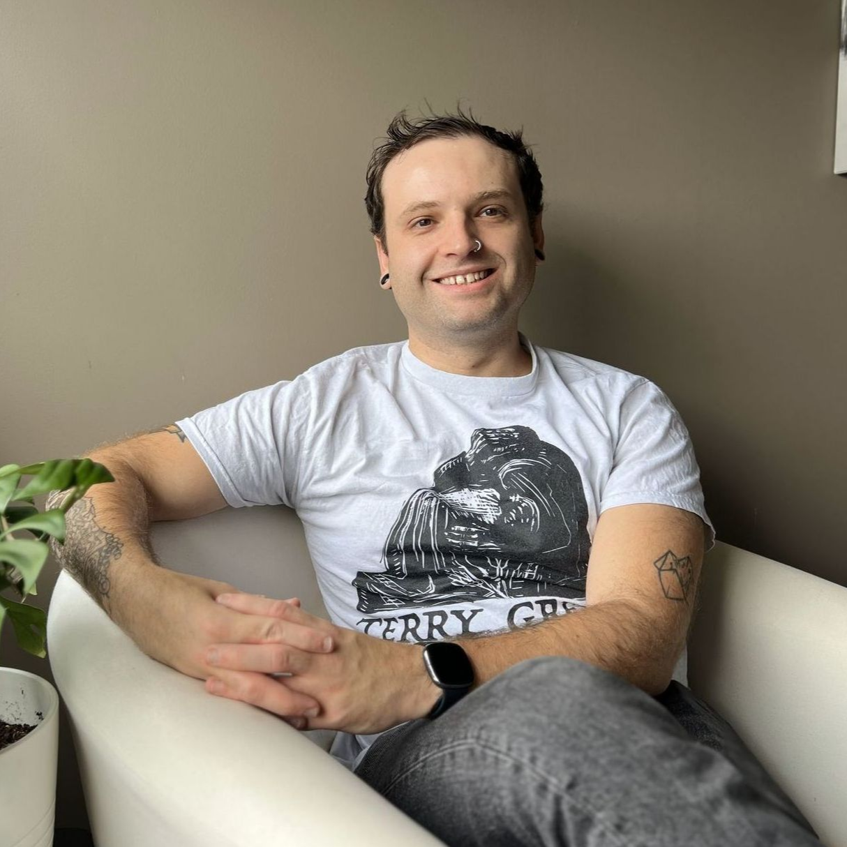 A man in a black sweater is sitting in a white chair with his hands folded