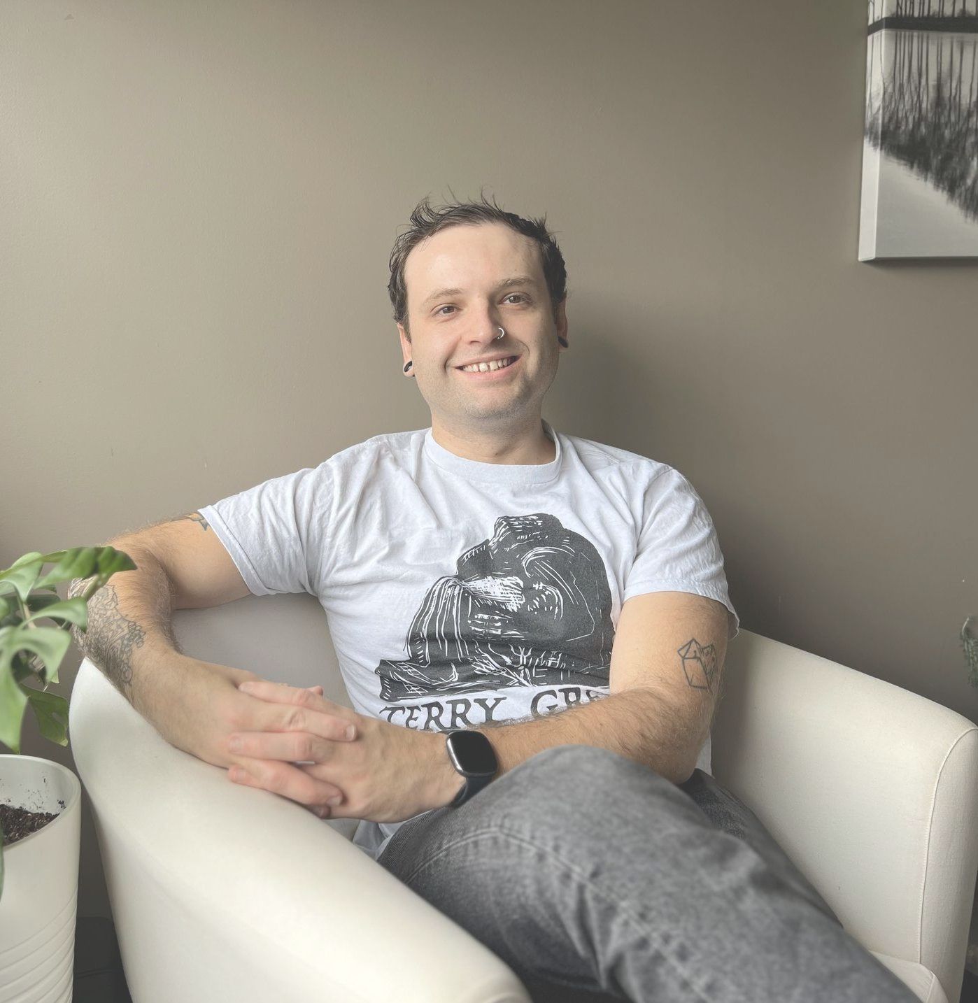 A man wearing a white t-shirt with tattoos sitting in a chair