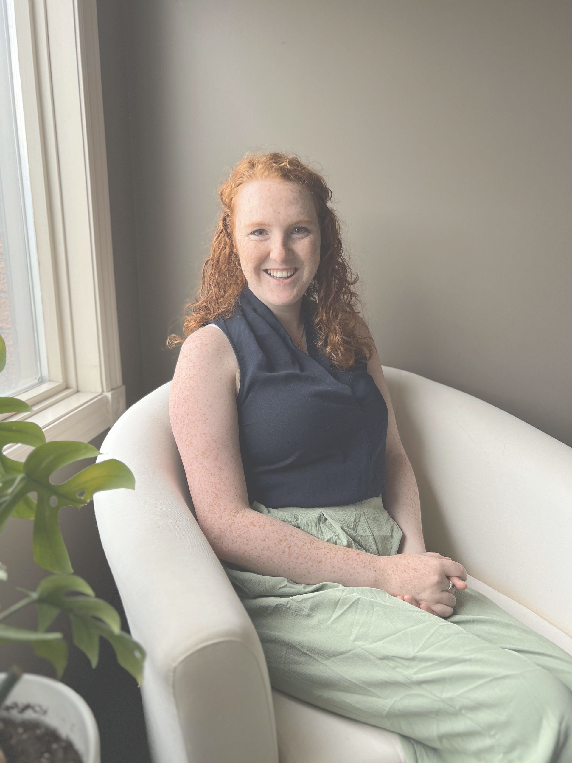 A woman in a blue shirt is sitting in a red chair and smiling.