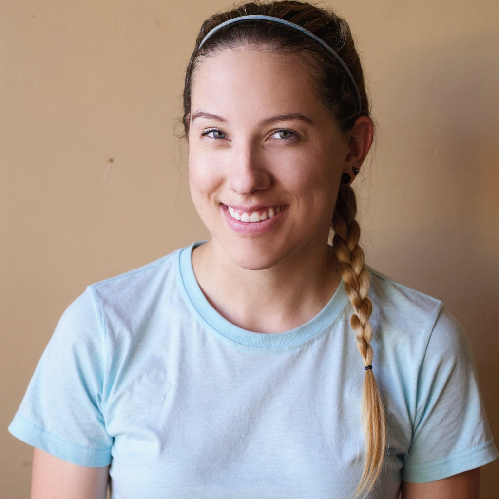 A woman wearing a blue tie dye shirt and a necklace is smiling.