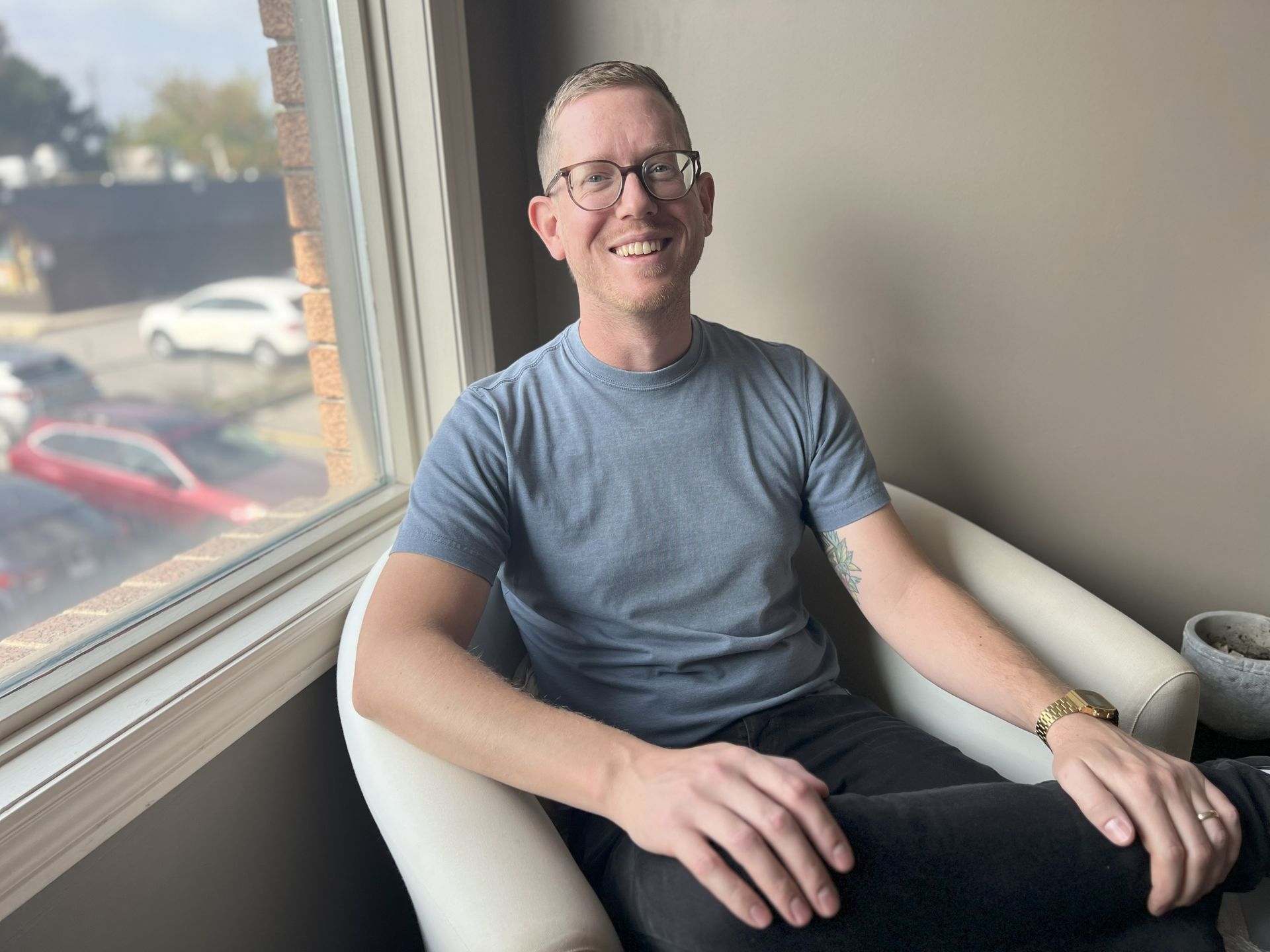 A man is sitting in a chair with his legs crossed and smiling.