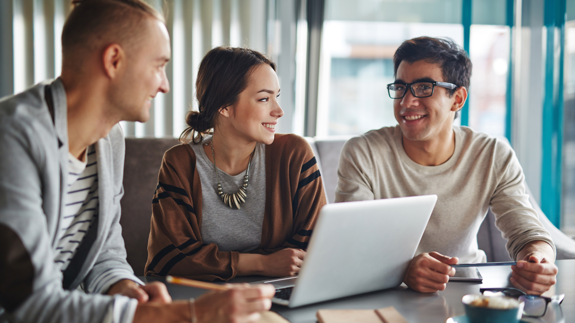 A group of people are sitting at a table looking at a laptop computer.