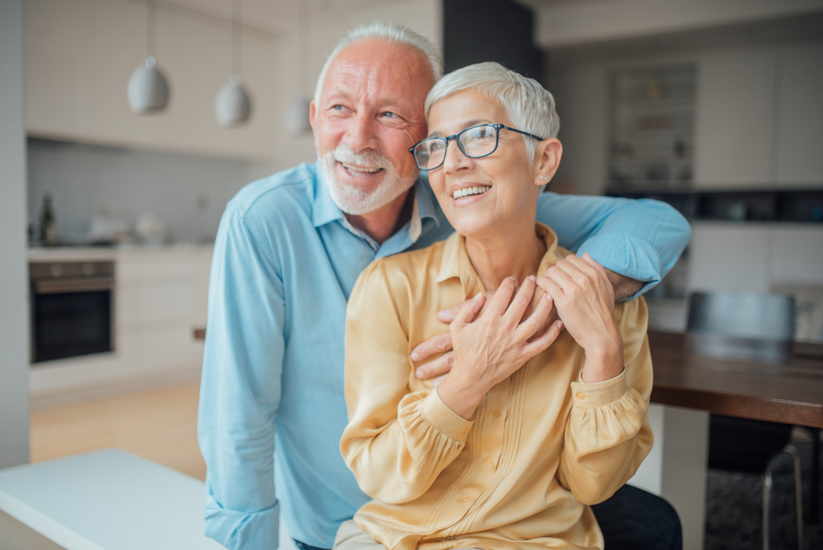 An elderly couple is posing for a picture in a kitchen.