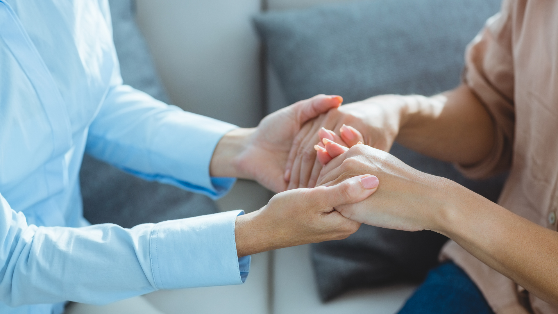 A woman is holding another woman 's hand while sitting on a couch.