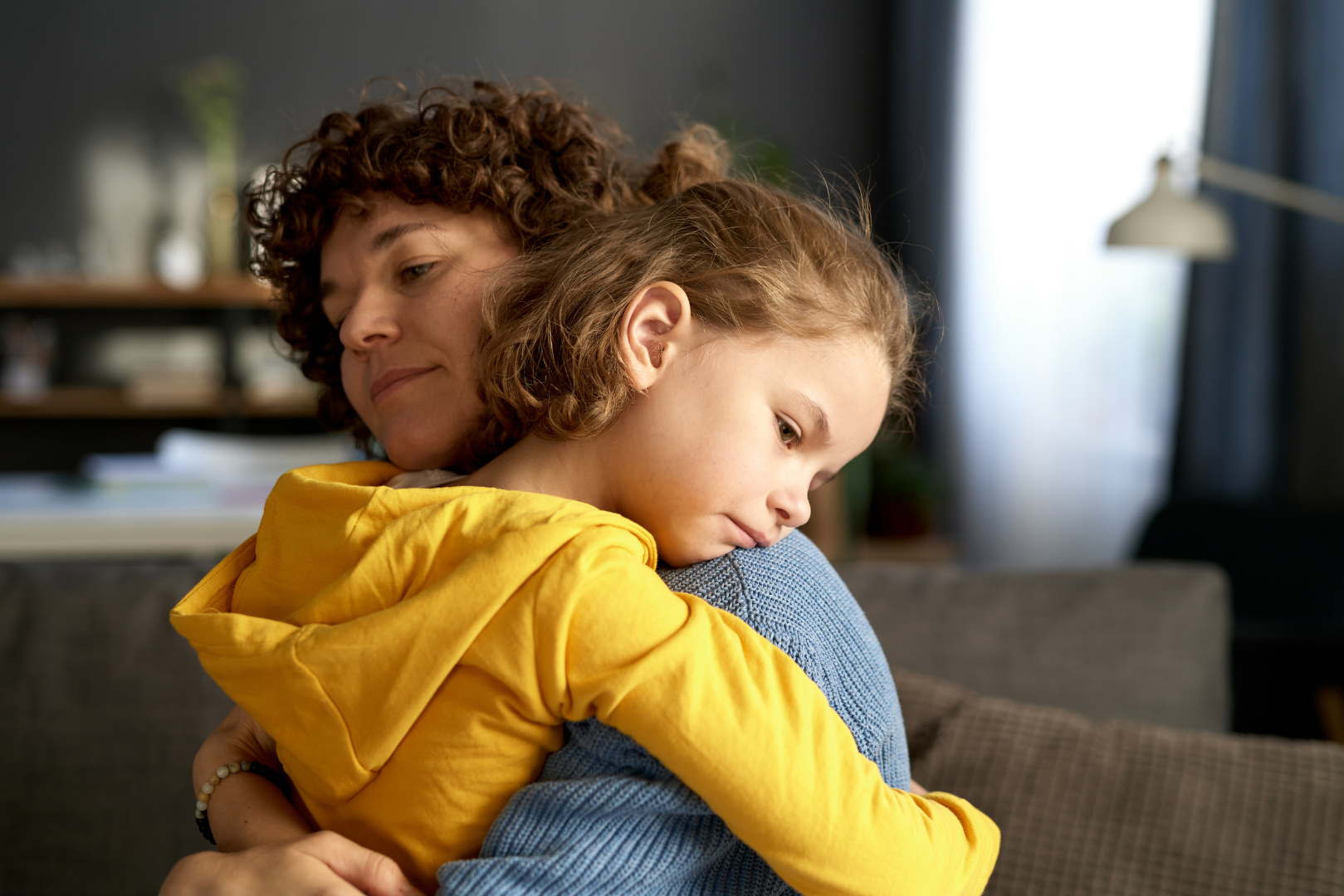 A woman is hugging a little girl on a couch.