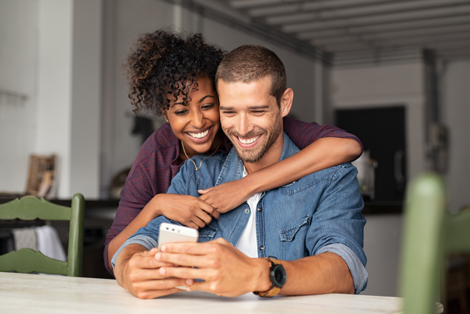 A man and a woman are sitting at a table looking at a cell phone.