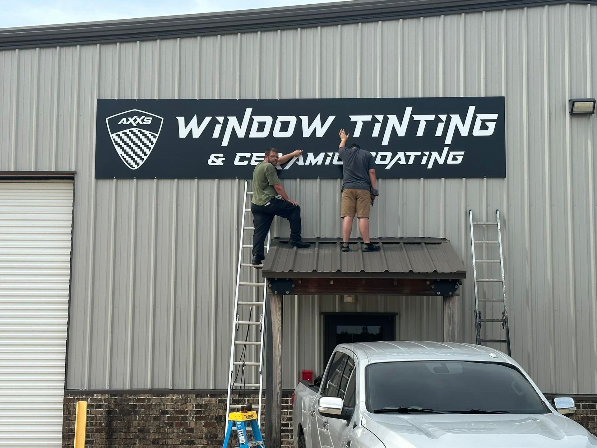 Two men are working on a sign for window tinting and ceramic coating.