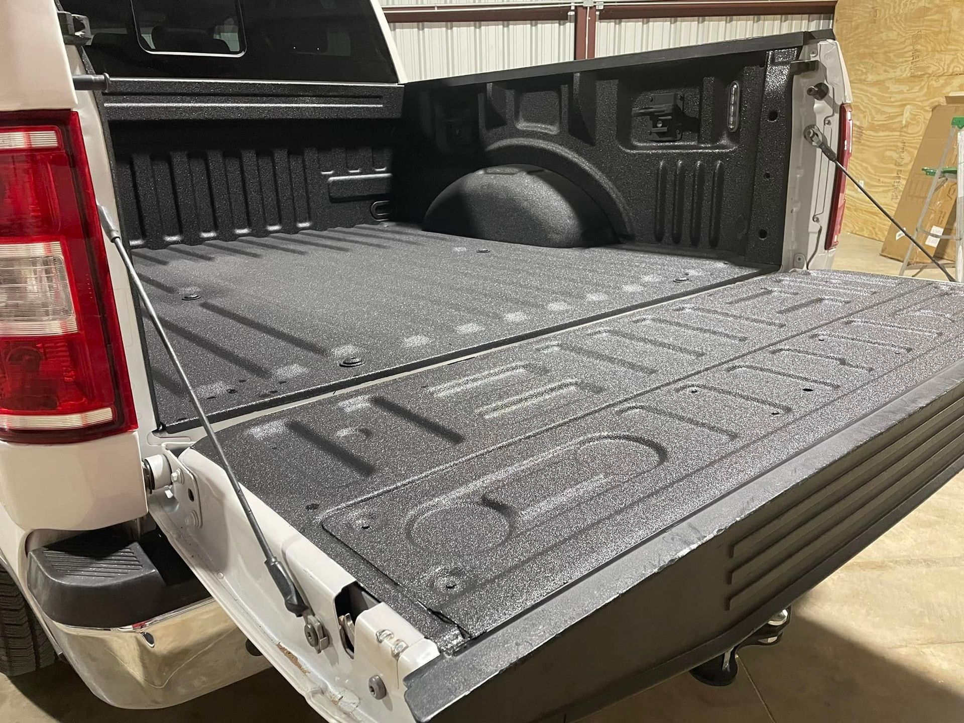 A white truck with a black bed is parked in a garage.