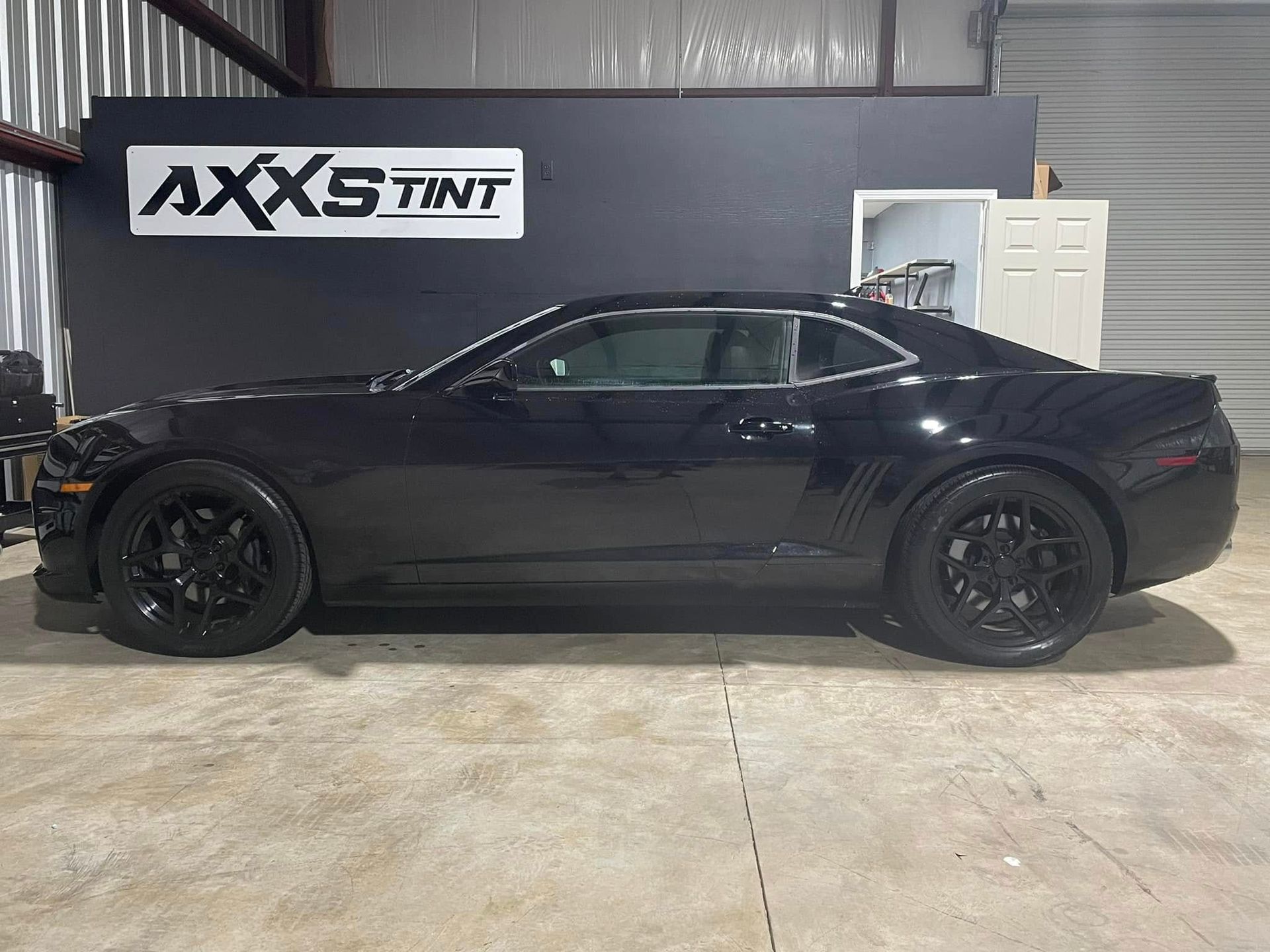 A black car is parked in a garage in front of a sign that says axs tint.