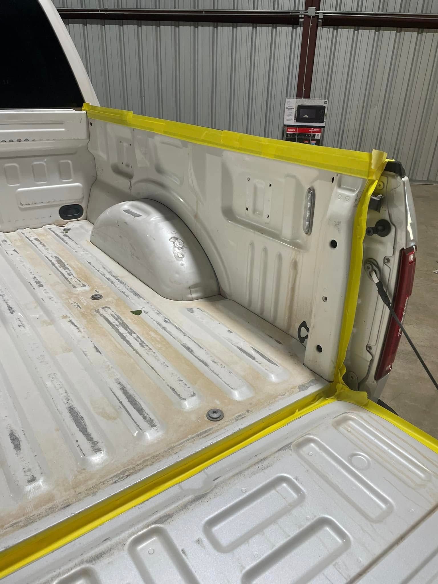 A white truck with a yellow tape covering the bed is sitting in a garage.
