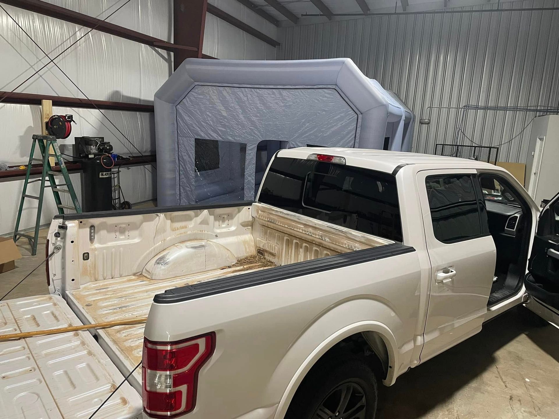 A white truck is parked in a garage next to an inflatable tent.