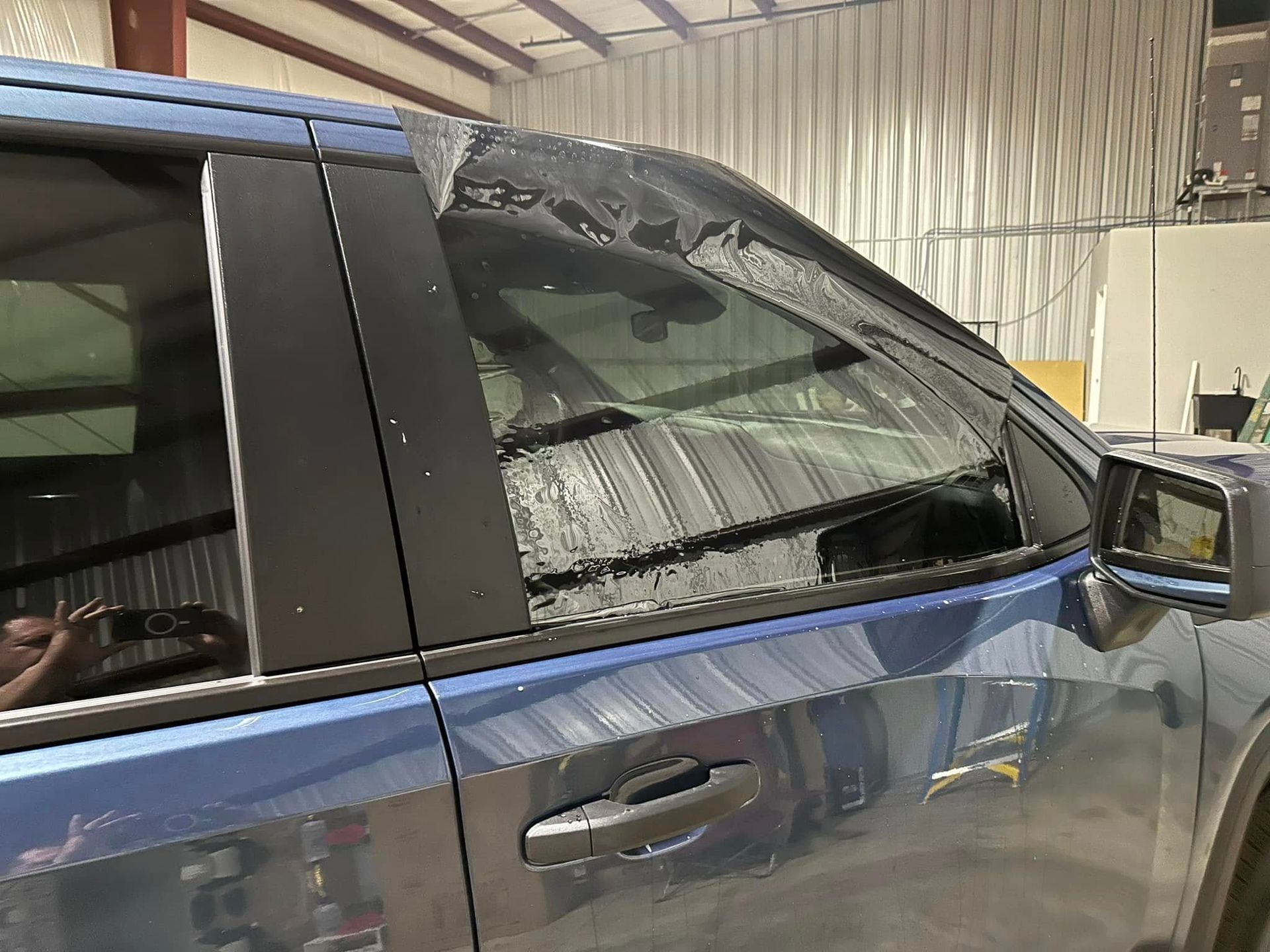A blue truck with a broken windshield is parked in a garage.