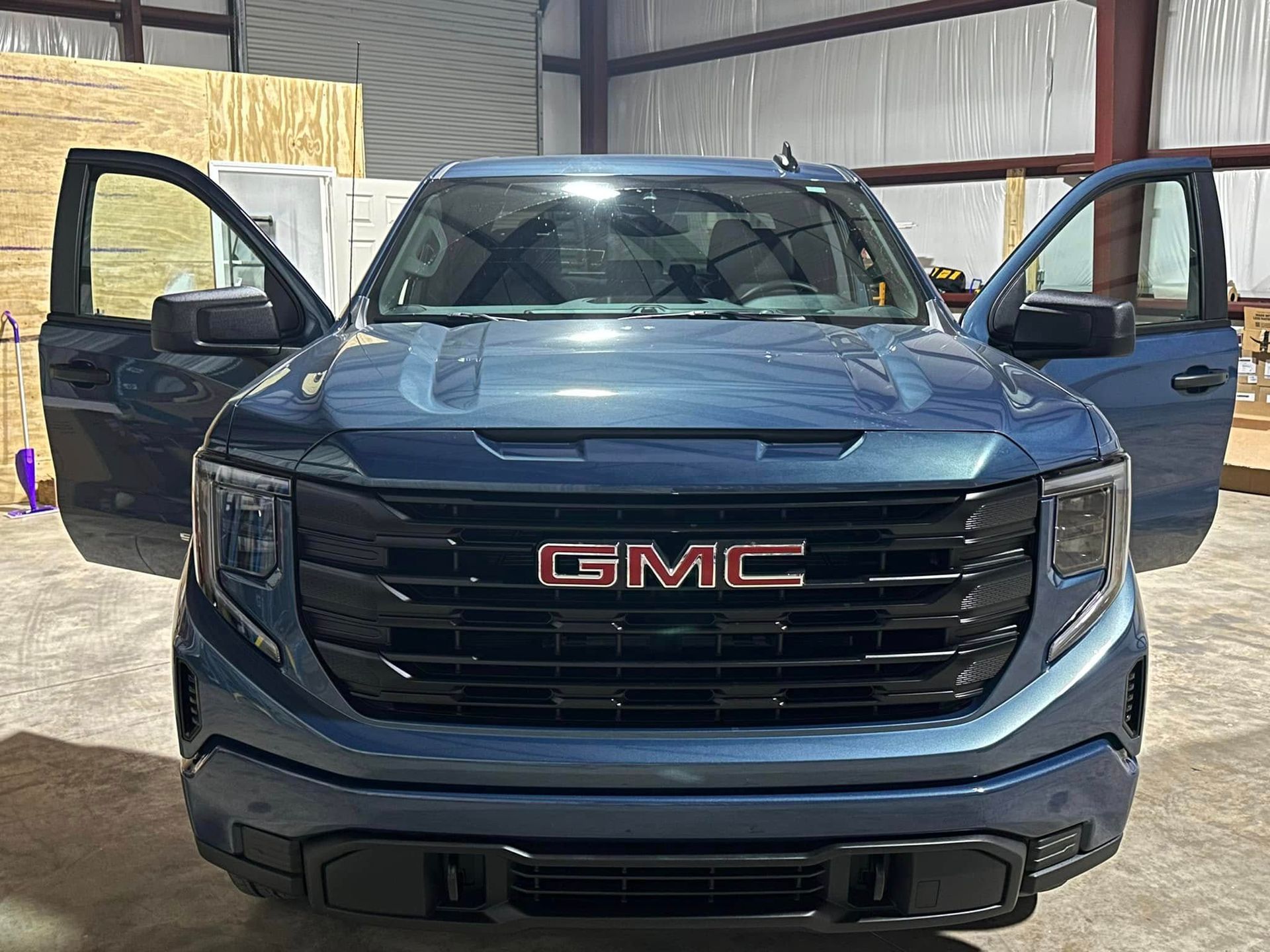 A blue gmc truck is parked in a garage with its doors open.