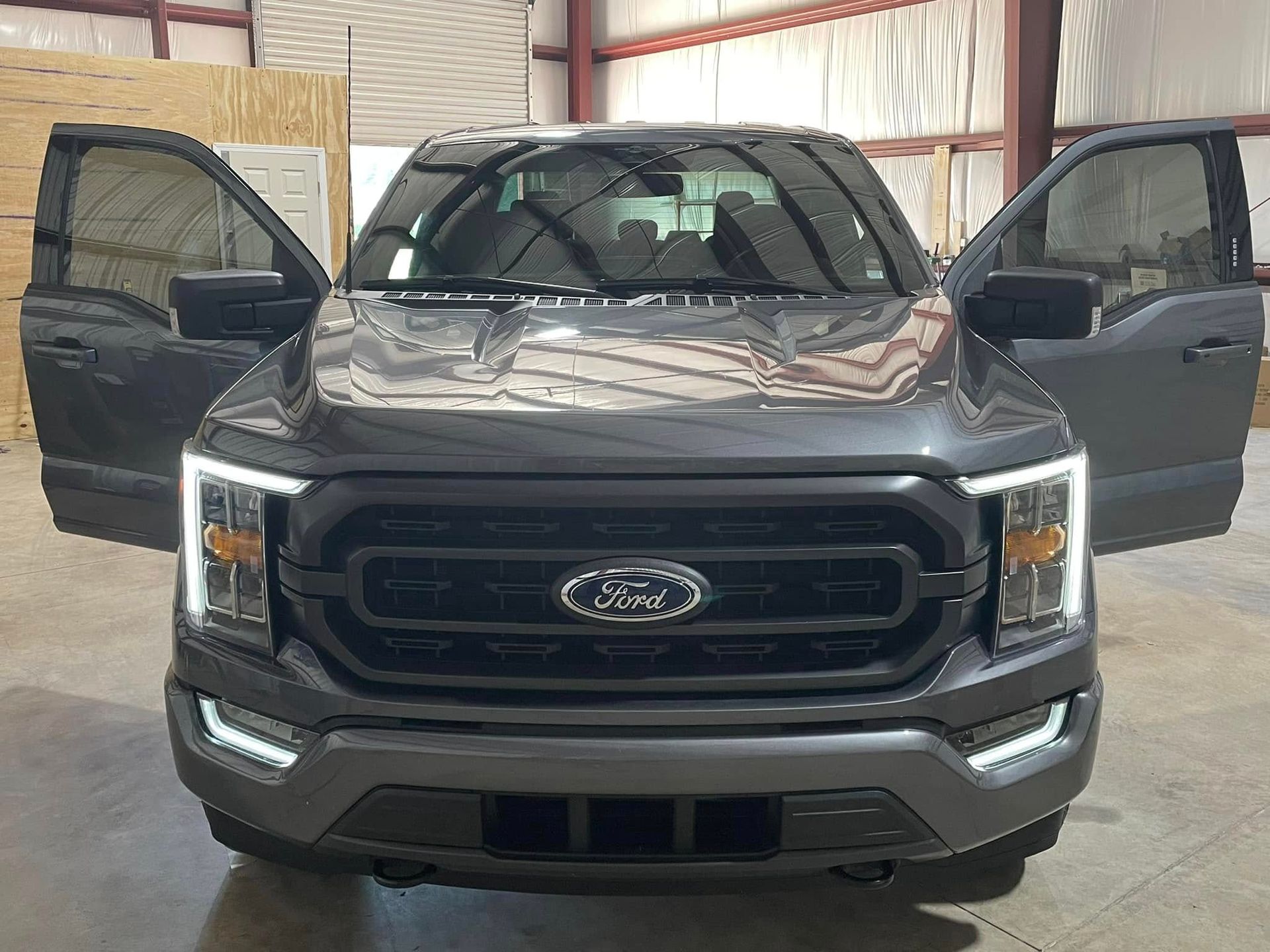 A black ford f150 truck is parked in a warehouse with its doors open.