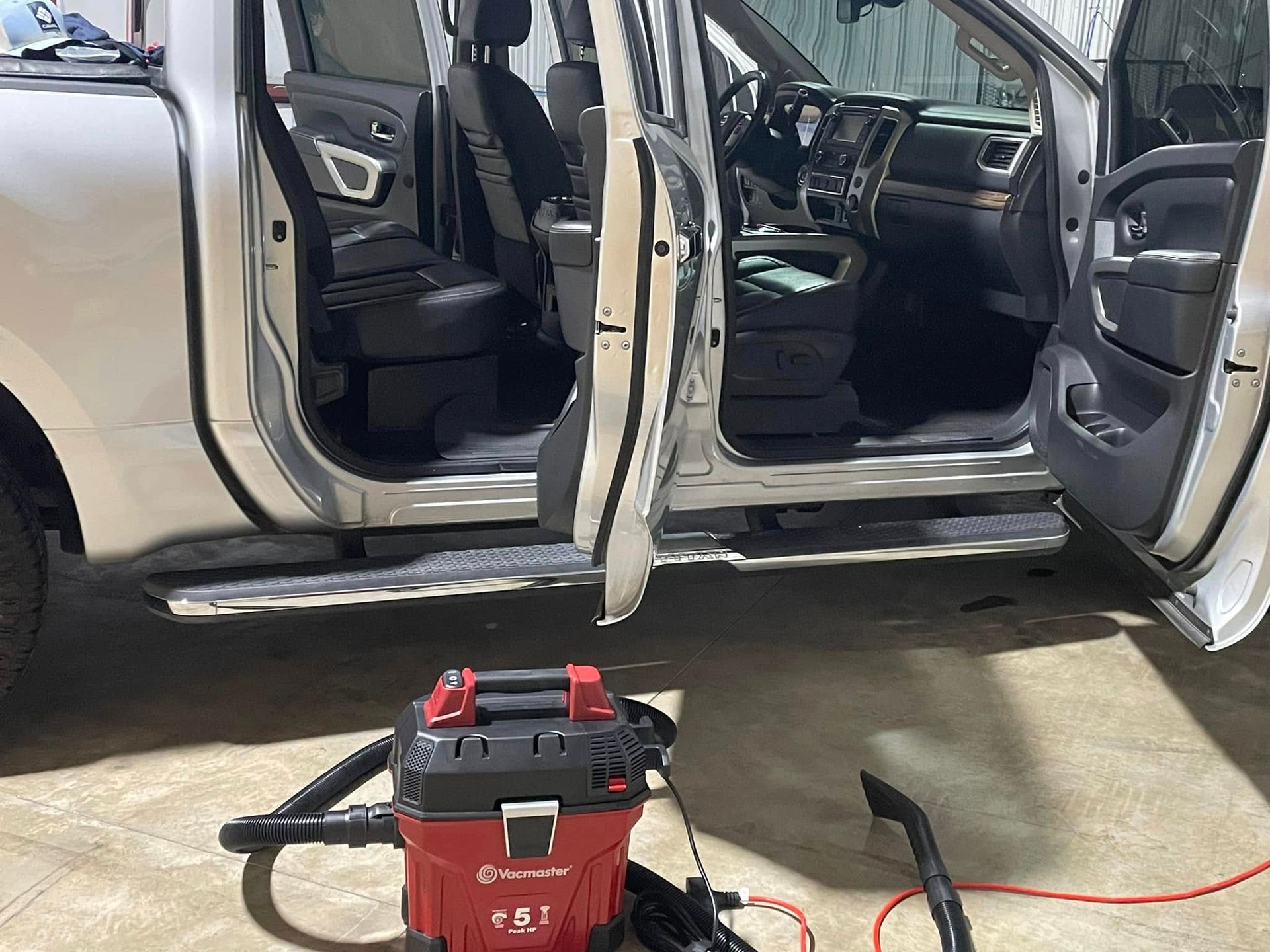 A vacuum cleaner is sitting next to a silver truck with its doors open.