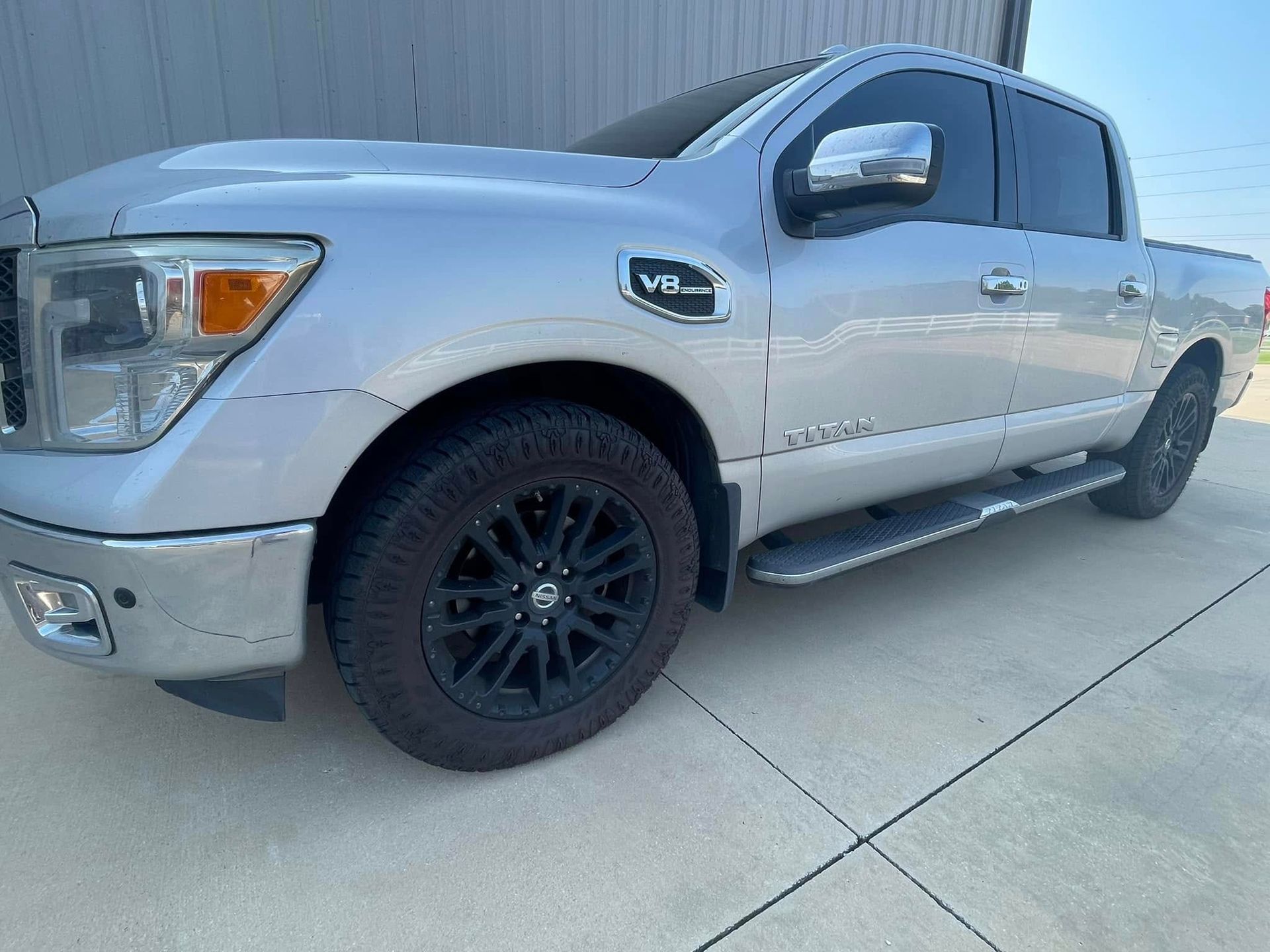 A silver pickup truck with black wheels is parked in a parking lot.