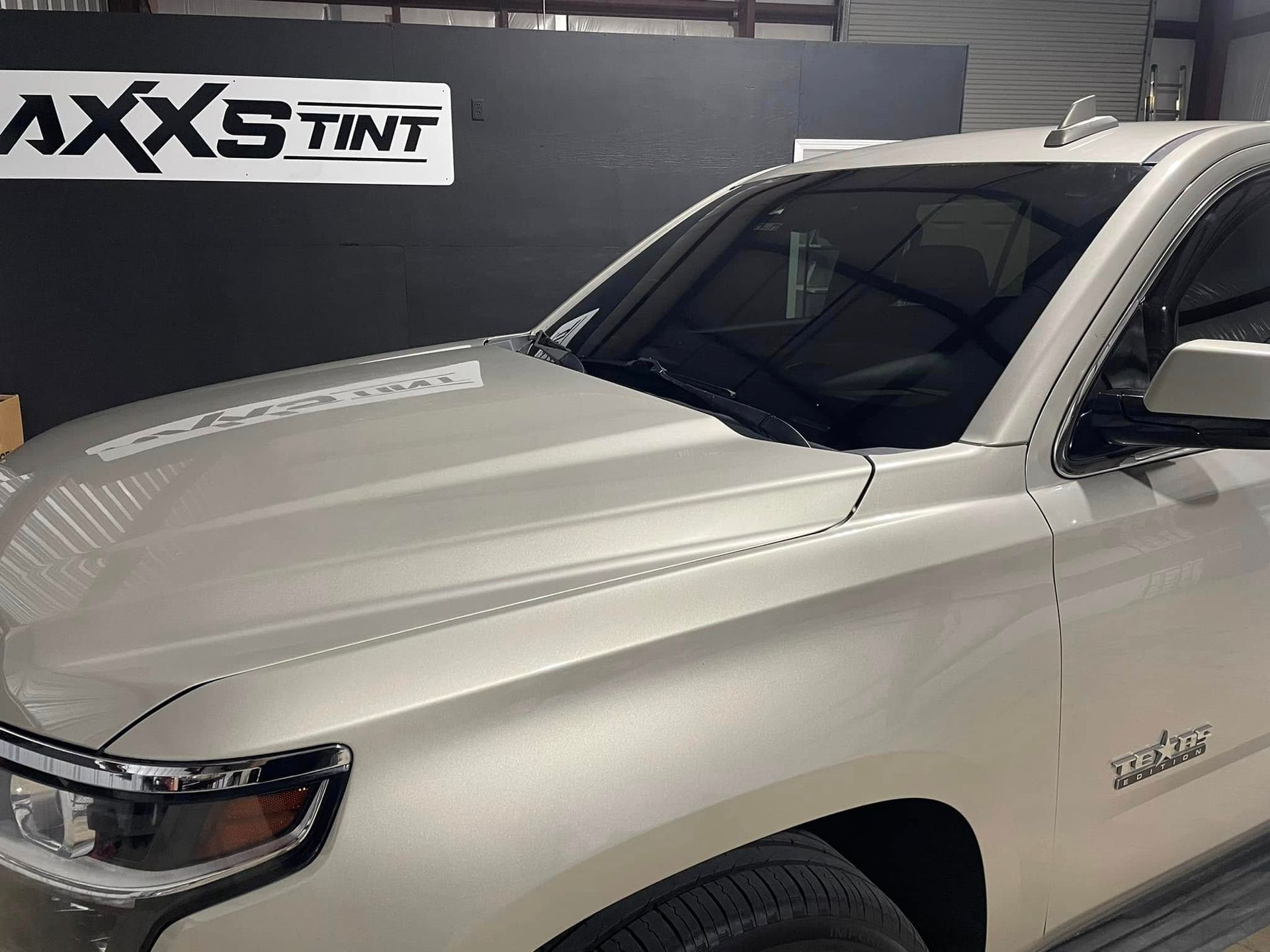 A white truck is parked in front of a sign that says axxs tint.