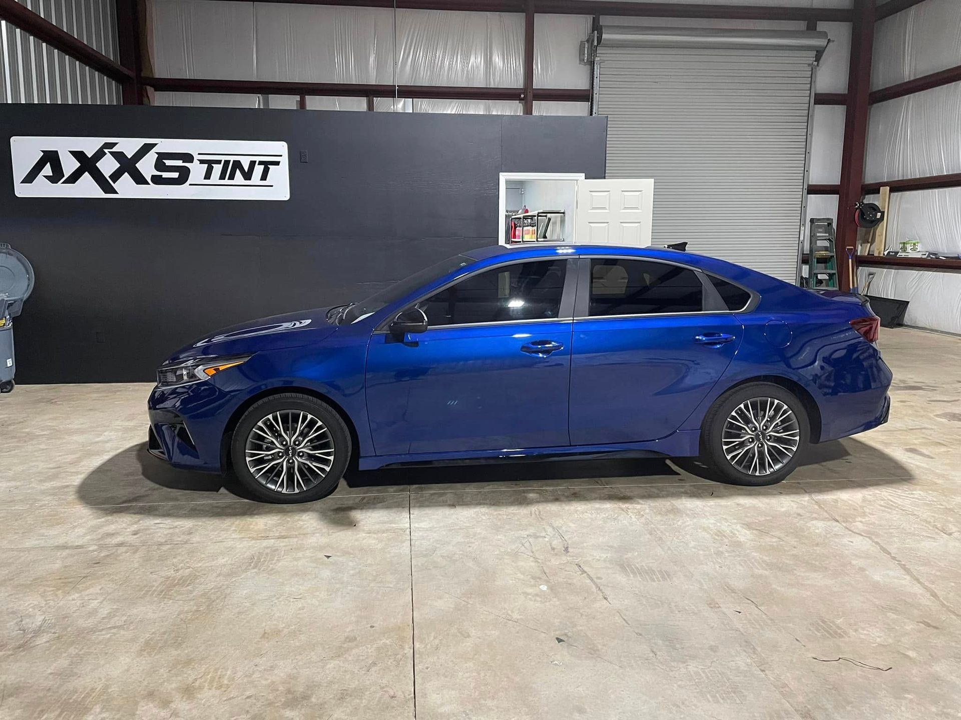 A blue car is parked in a garage next to a sign that says axs tint.