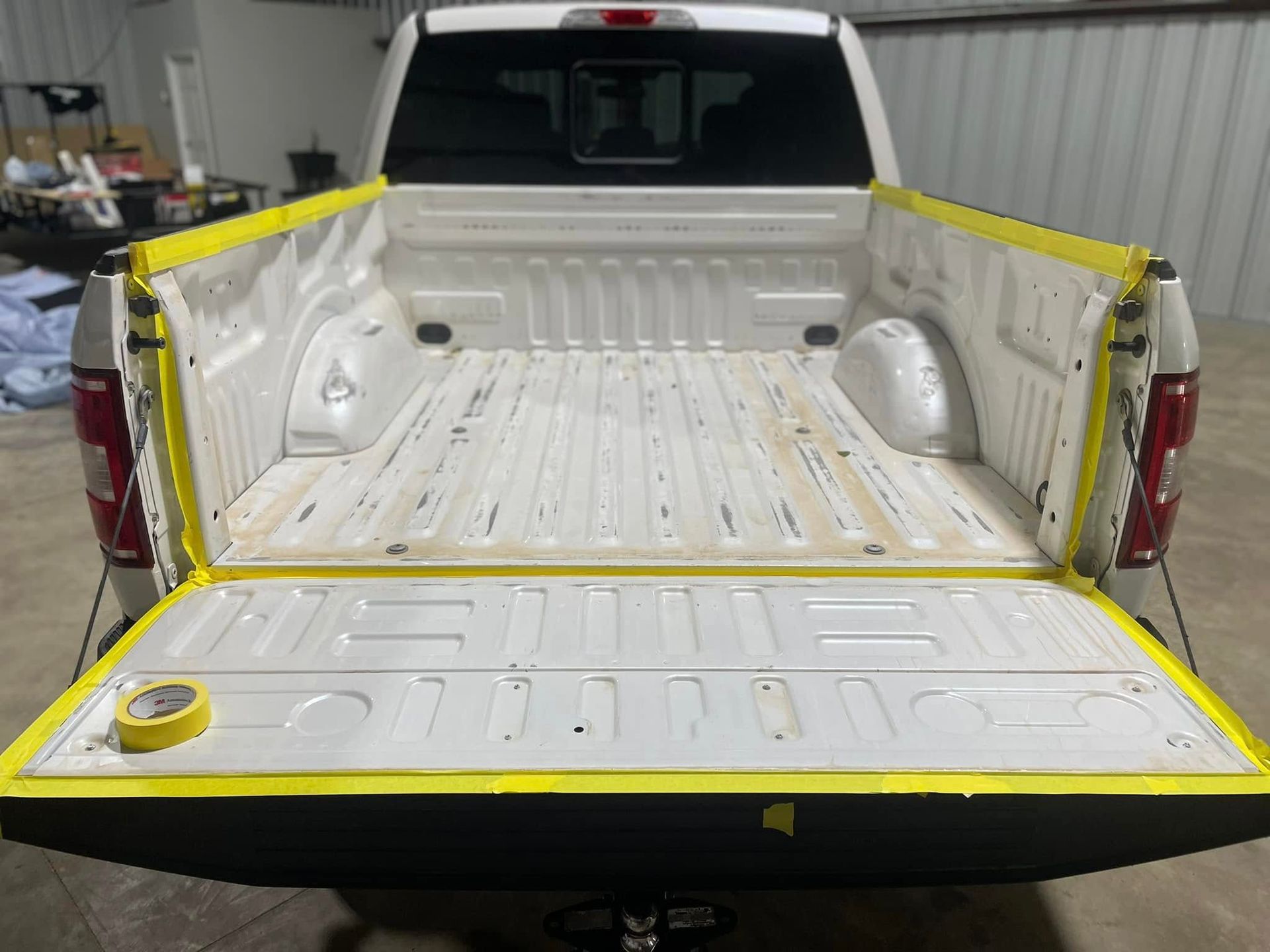 The back of a white truck is being painted with yellow tape.