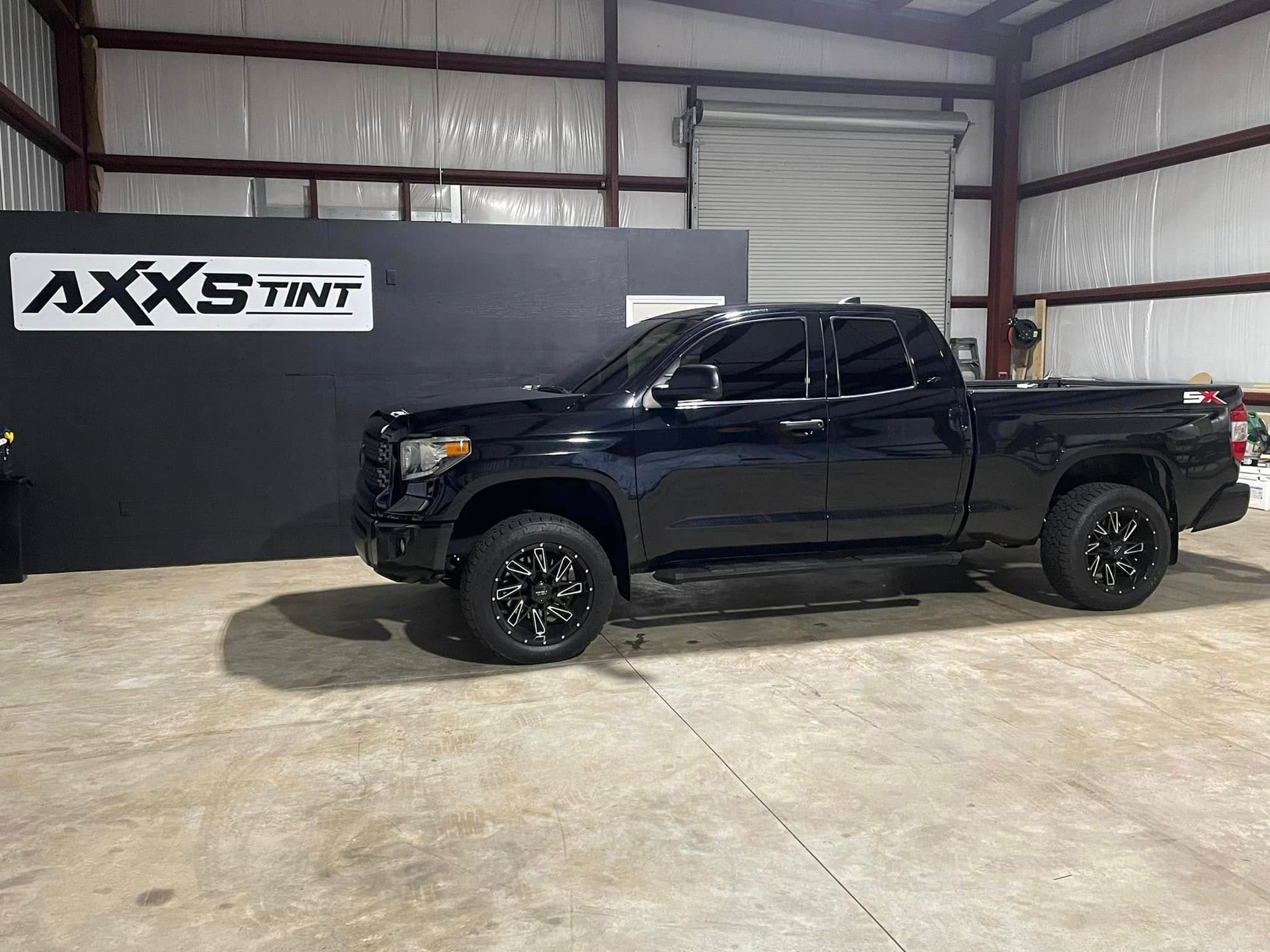 A black truck is parked in a garage next to a wall.