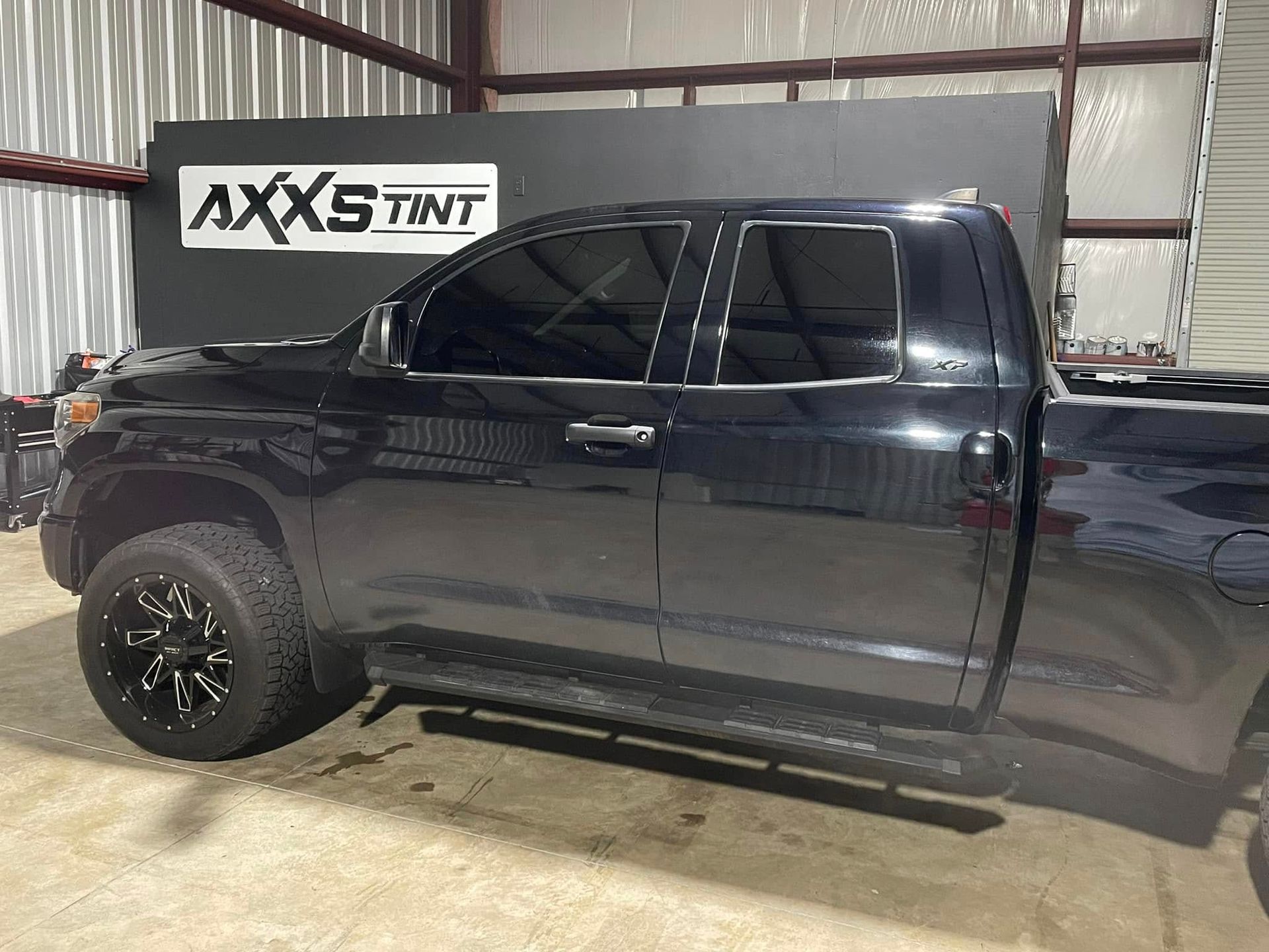 A black truck is parked in a garage in front of a sign that says axxs tint.