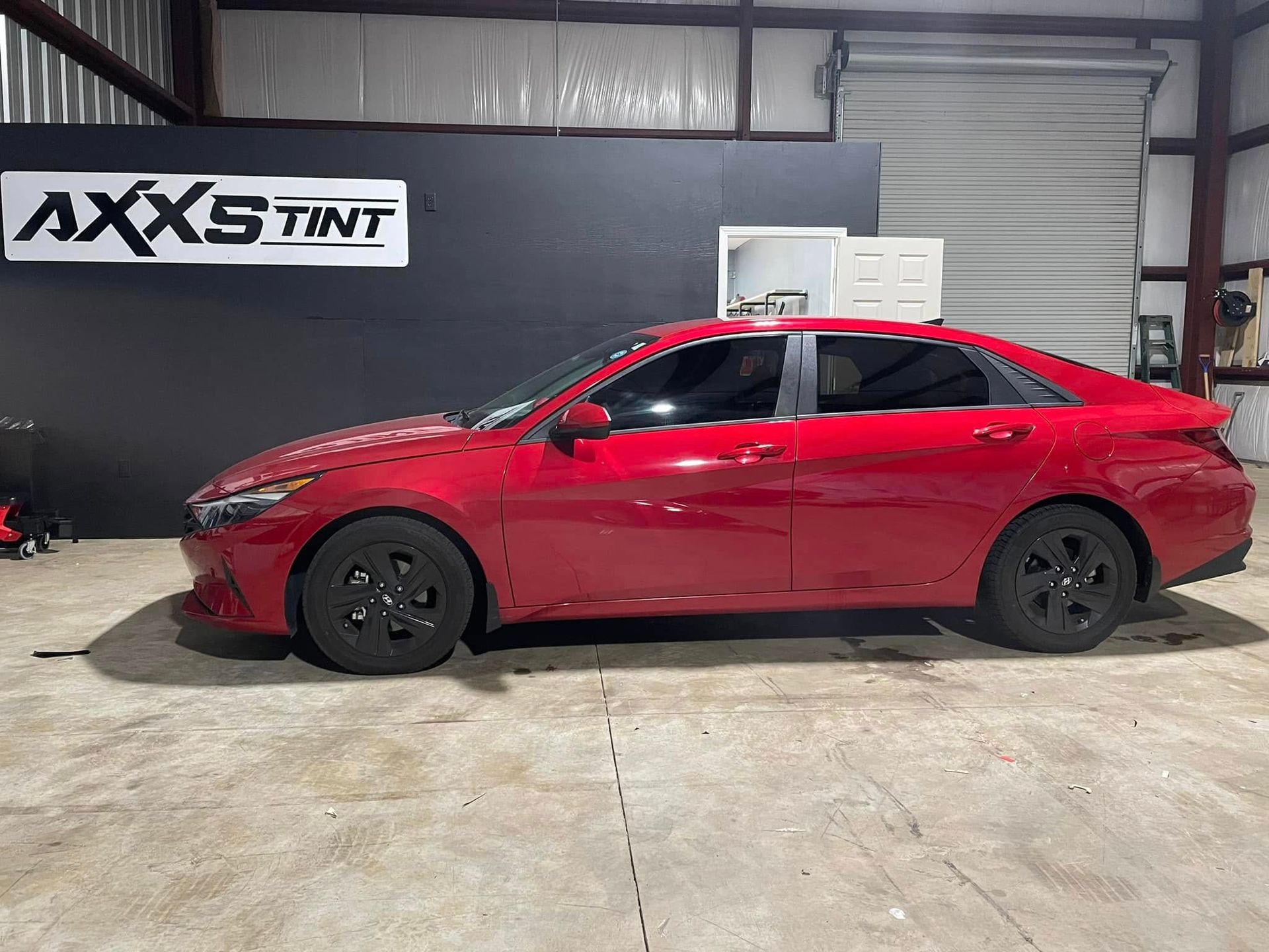 A red car is parked in a garage next to a sign that says axs tint.