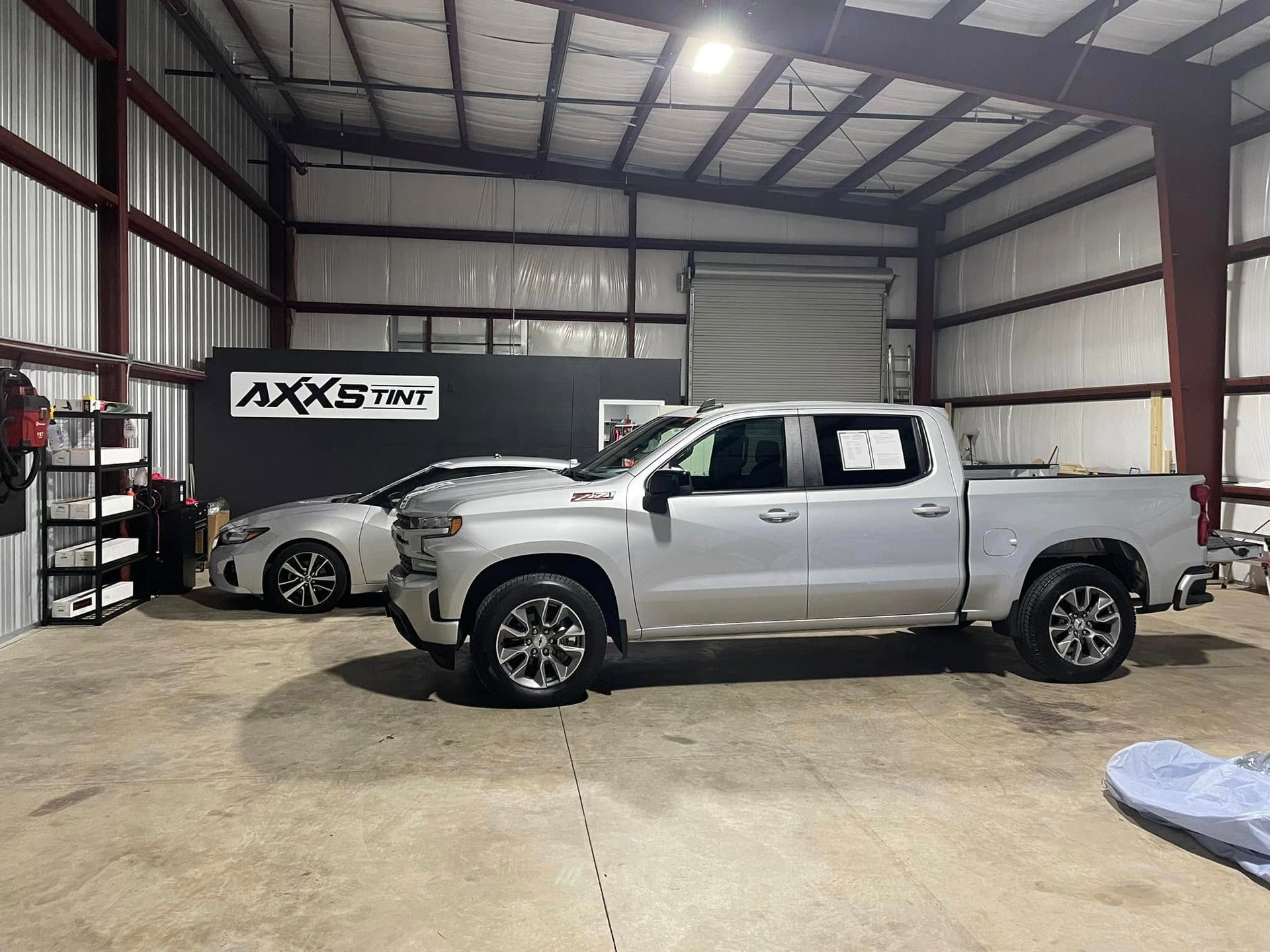 A silver truck is parked in a garage next to a white car.