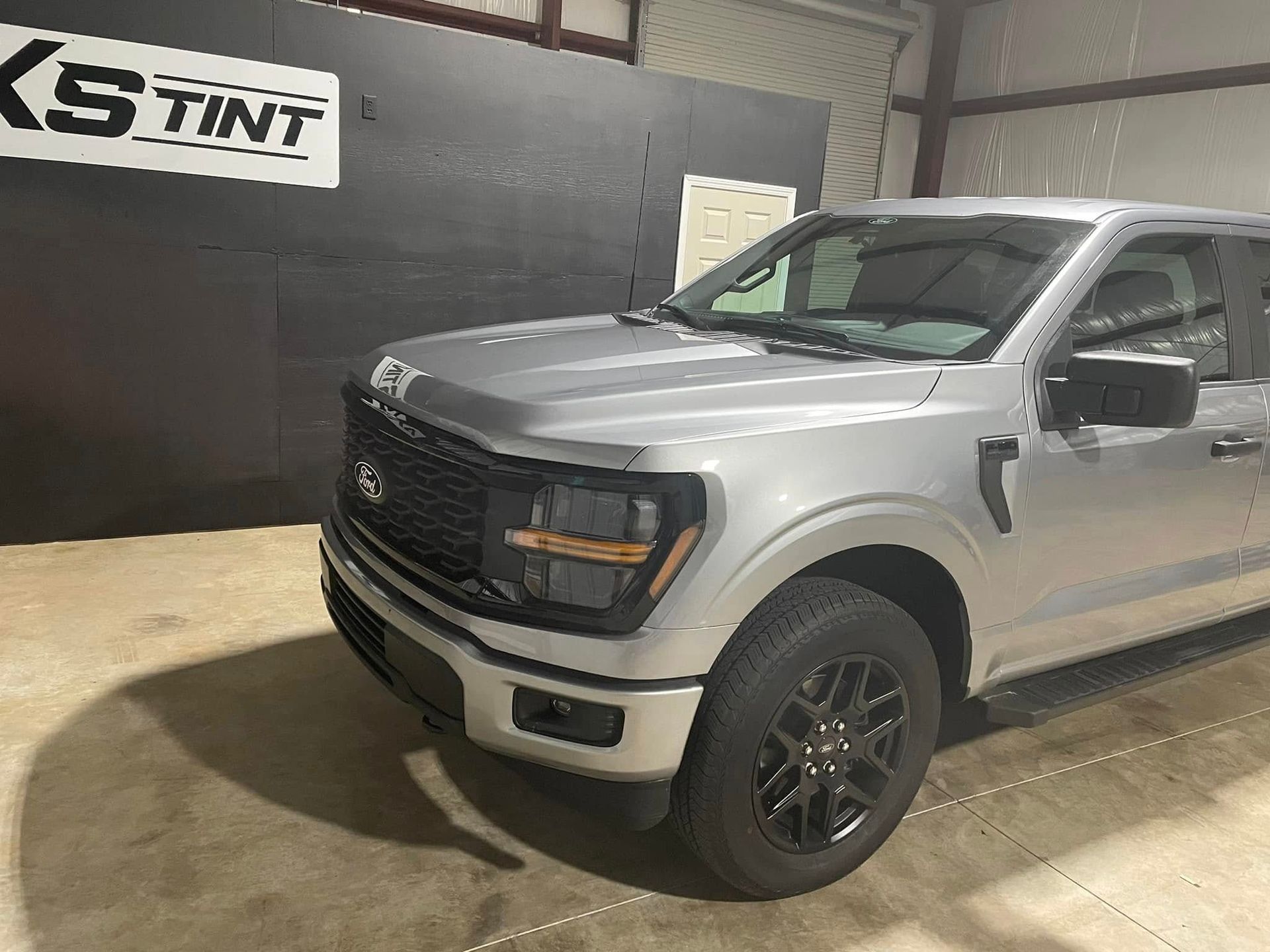 A silver truck is parked in a garage next to a sign that says ks tint.