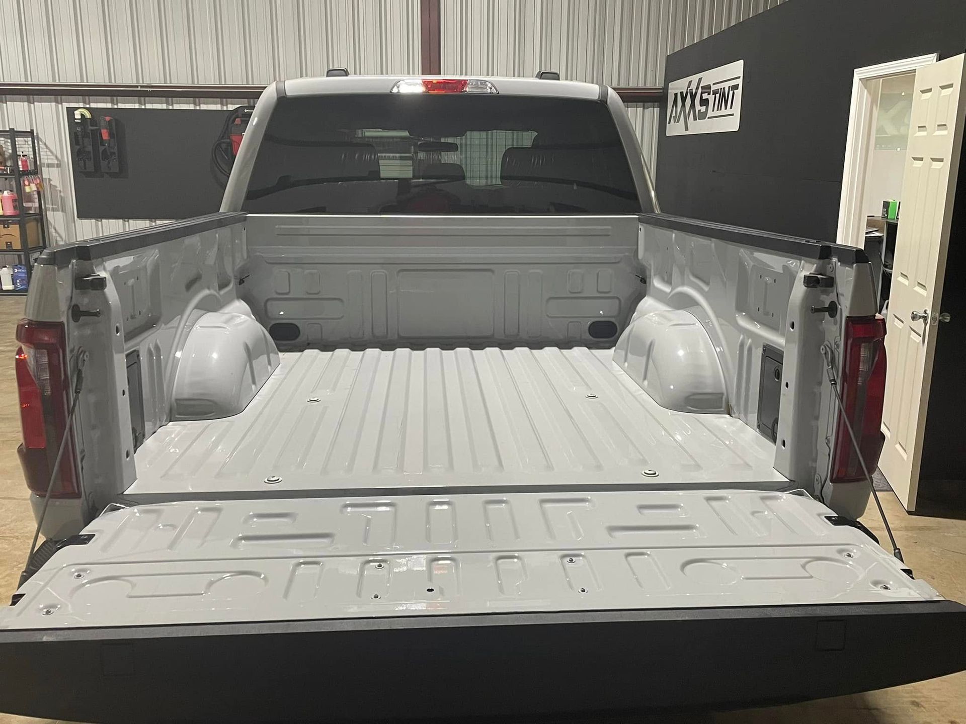 A white truck is parked in a garage with the bed open.
