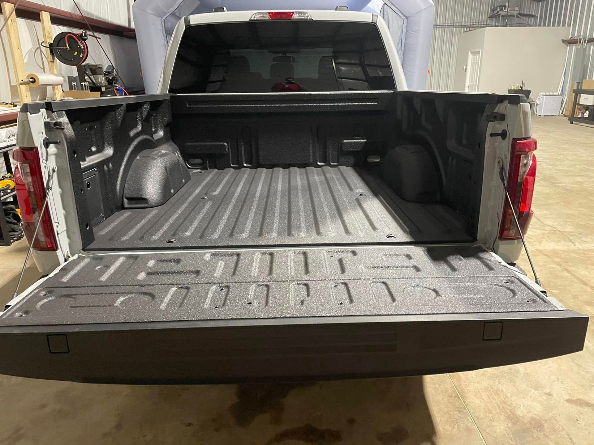 The back of a truck with the bed open is sitting in a garage.