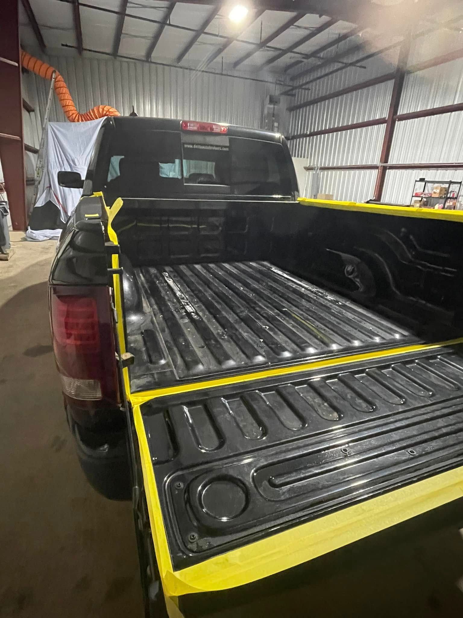 A black truck with yellow stripes on the bed is parked in a garage.
