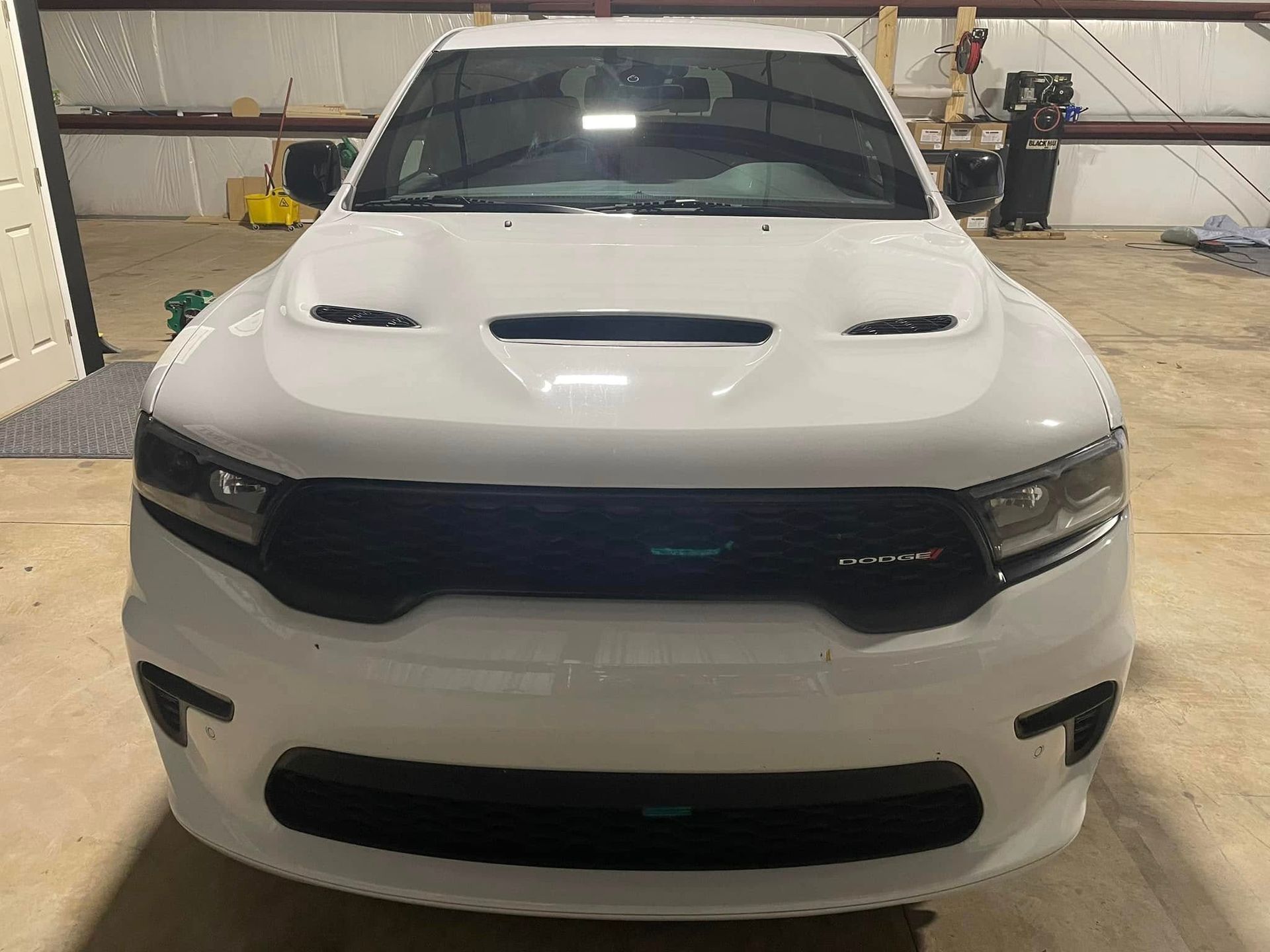 A white truck with a black hood is parked in a garage.
