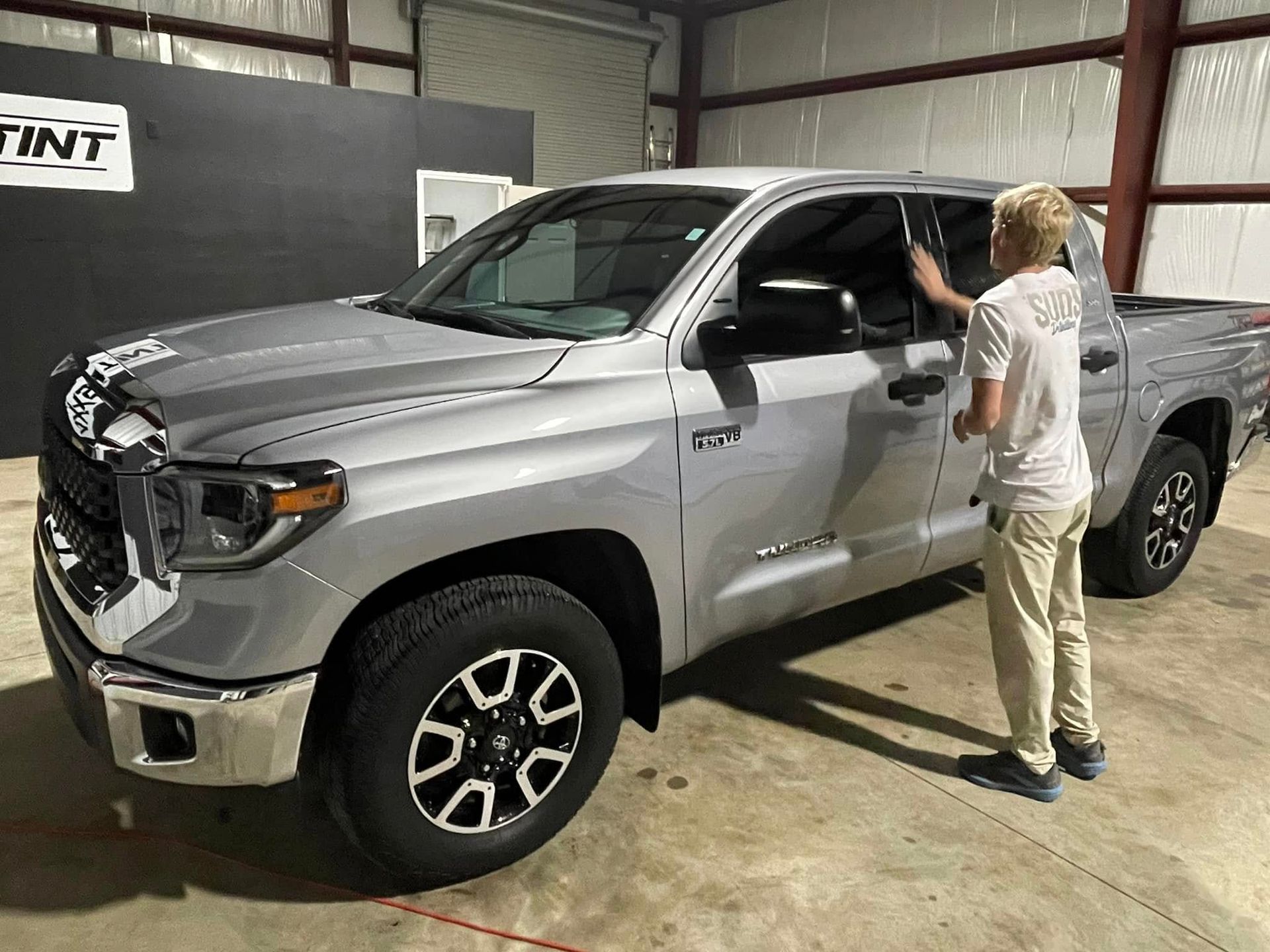 A man is standing next to a silver truck in a garage.