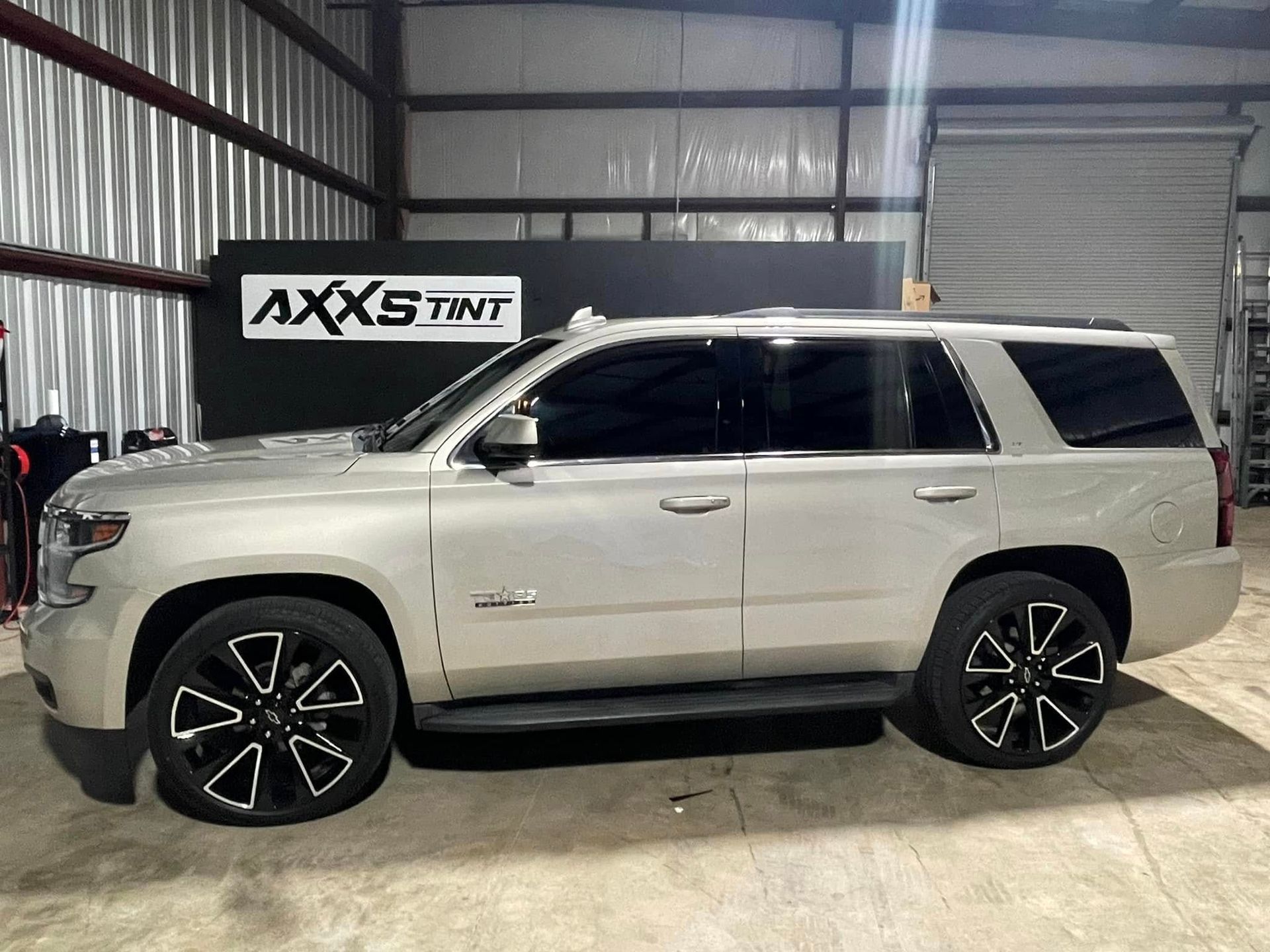A silver suv is parked in a garage next to a sign that says axs tint.
