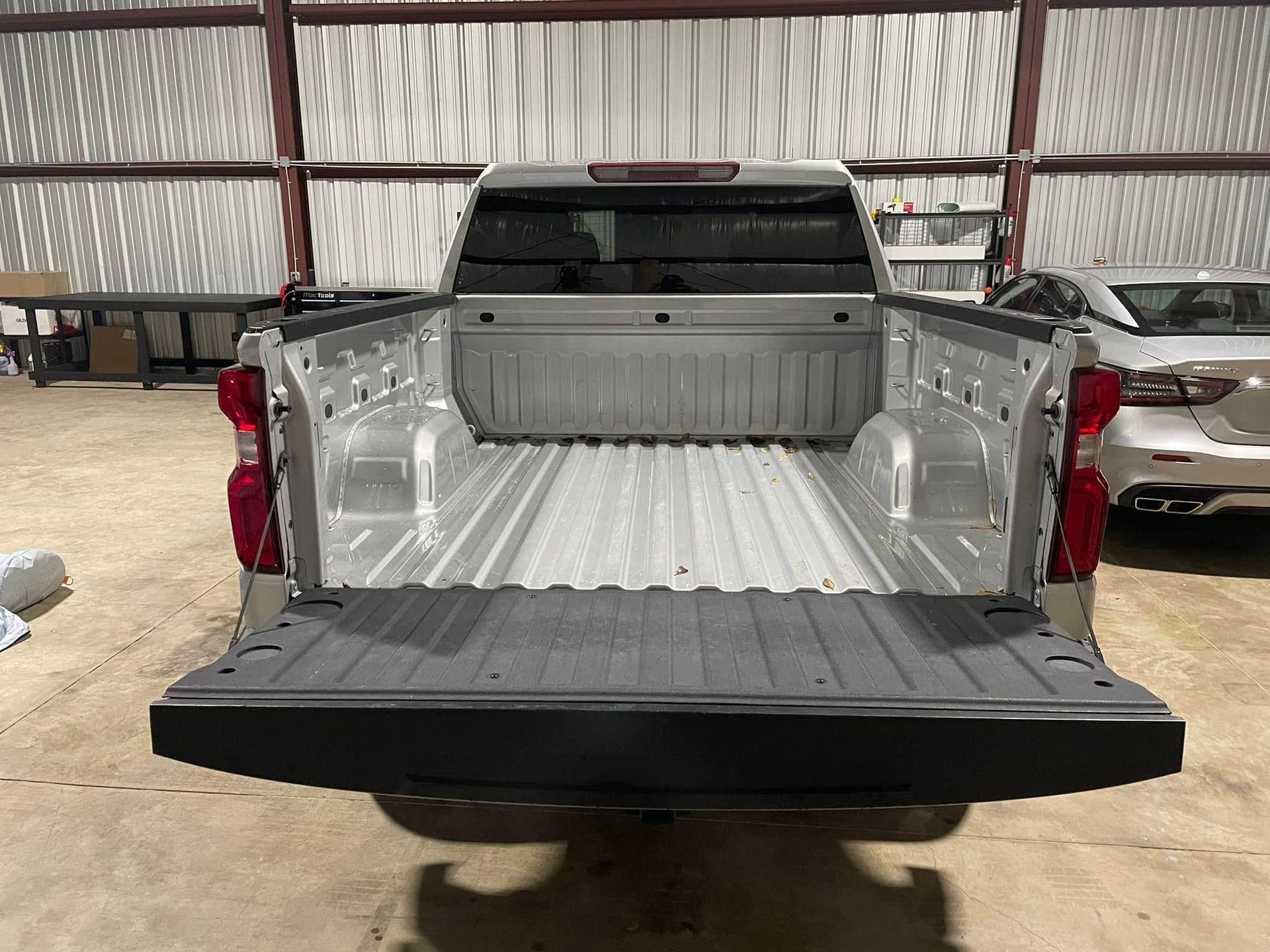 A silver truck is parked in a garage with its bed open.