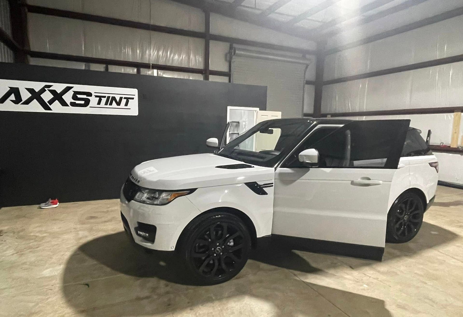 A white range rover sport is parked in a warehouse with its doors open.