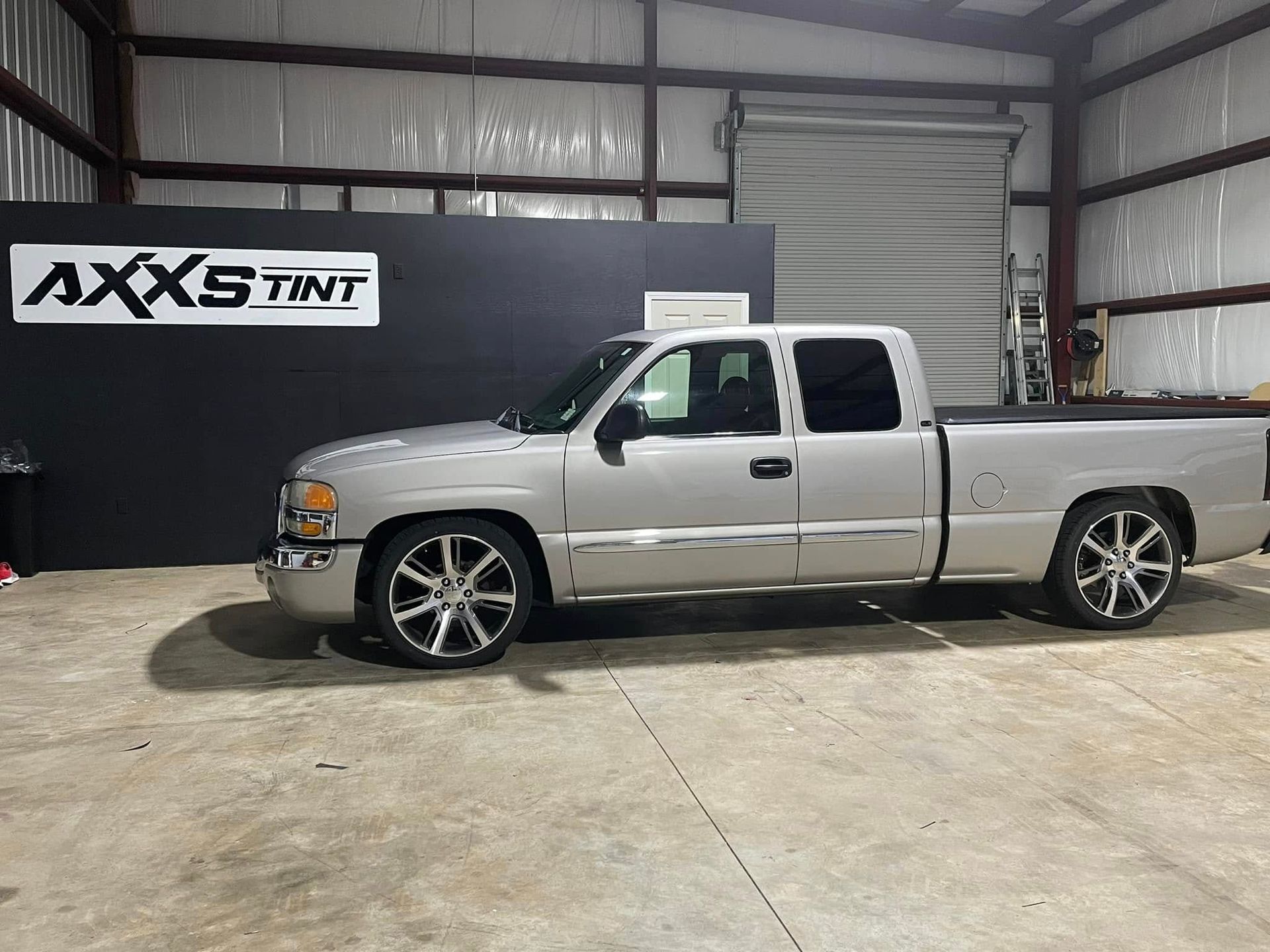 A silver truck is parked in a garage next to a sign that says axs tint.