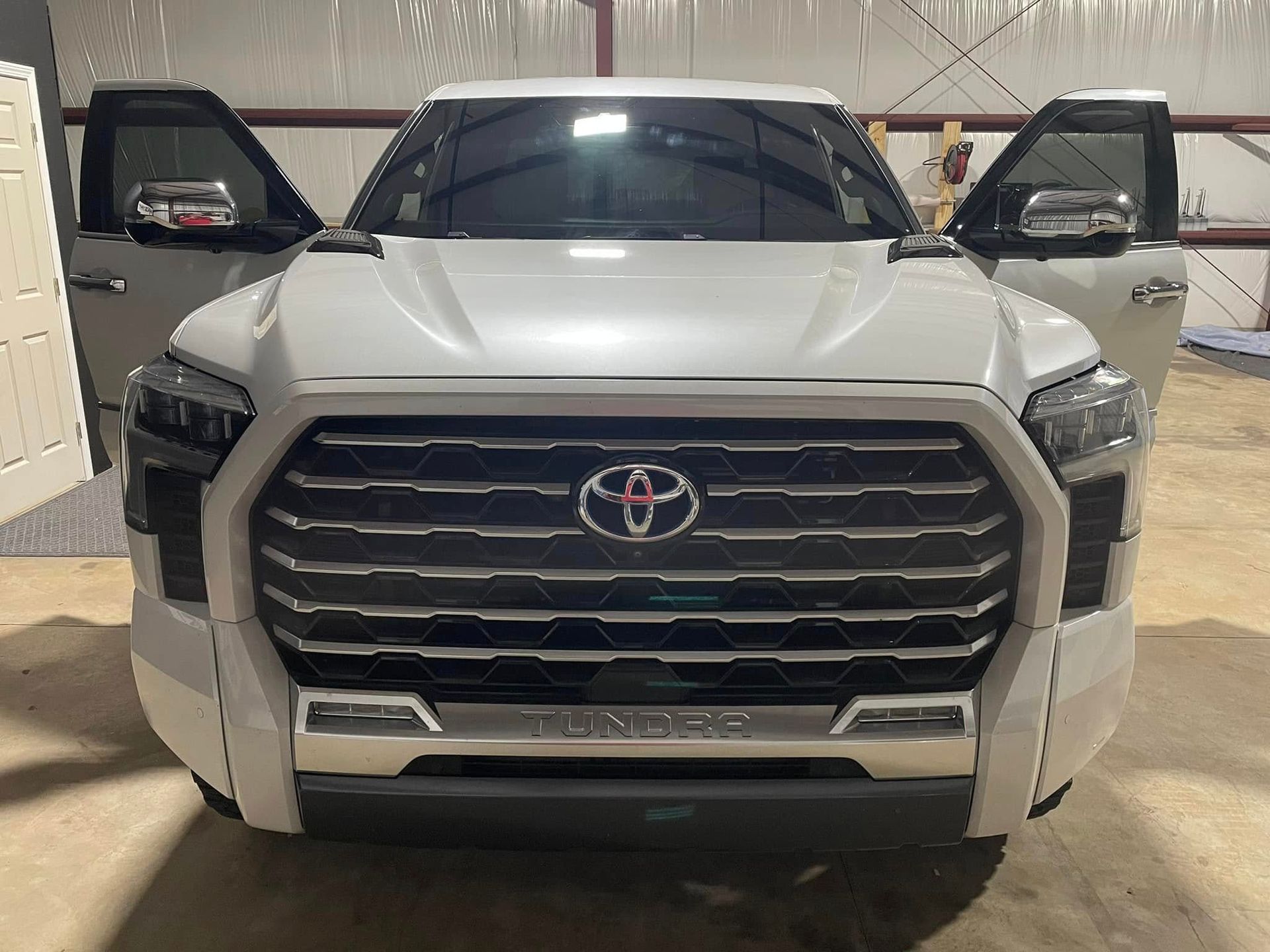 A white toyota tundra is parked in a garage with its doors open.