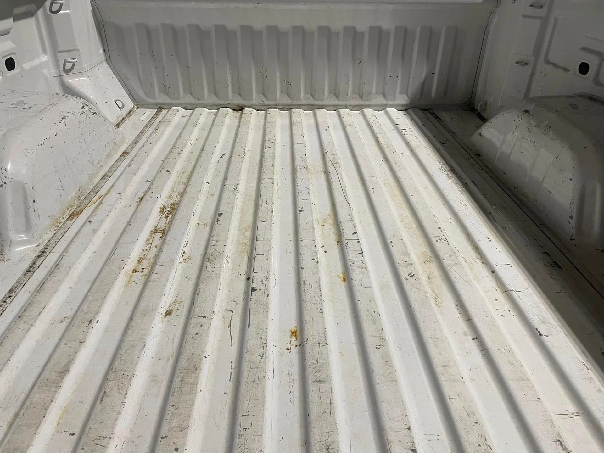 The bed of a white truck is empty and dirty.