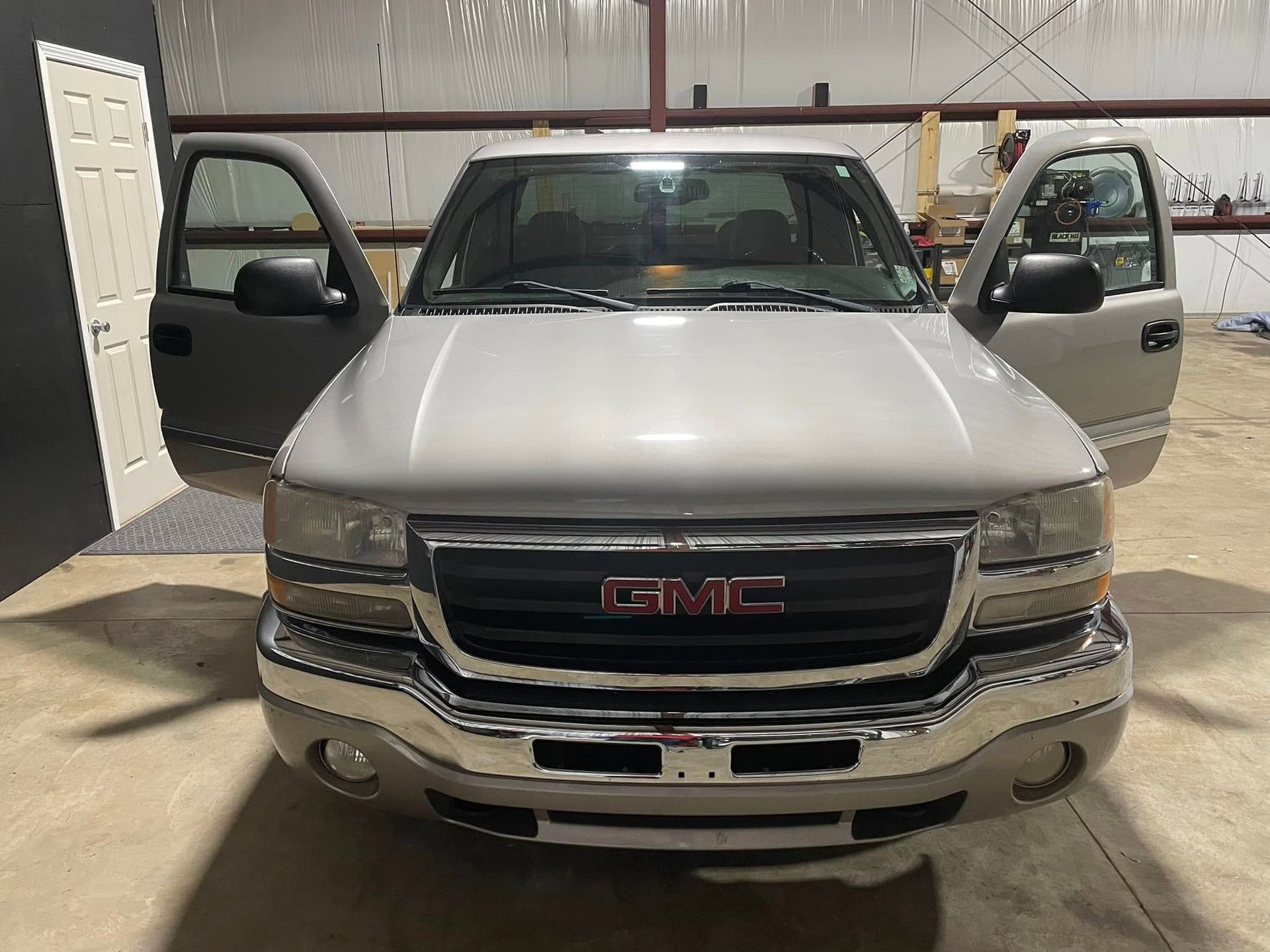 A silver gmc truck is parked in a garage with its doors open.